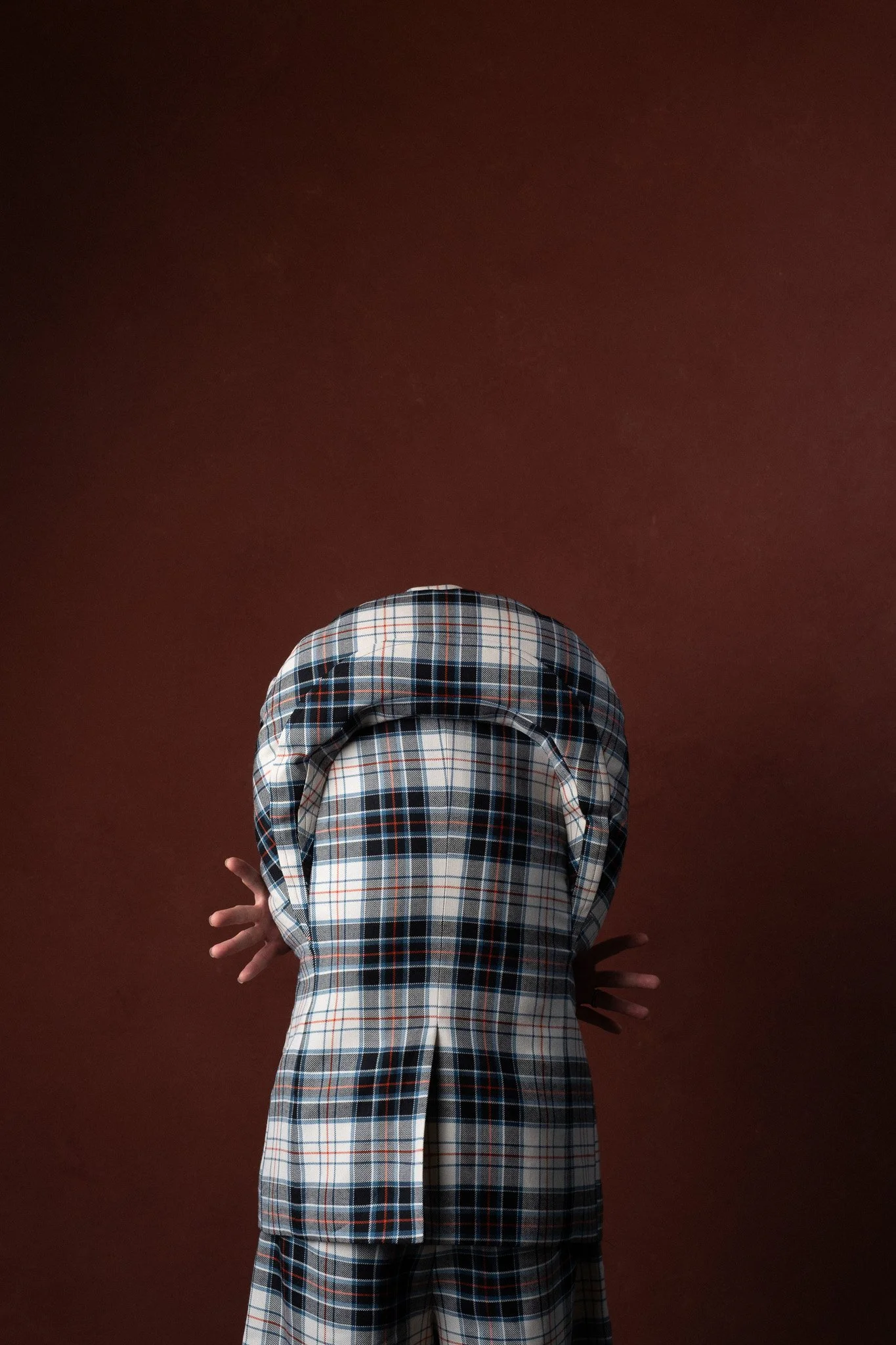 Person with a checkered shirt and pants, arms crossed, standing against a brown background.