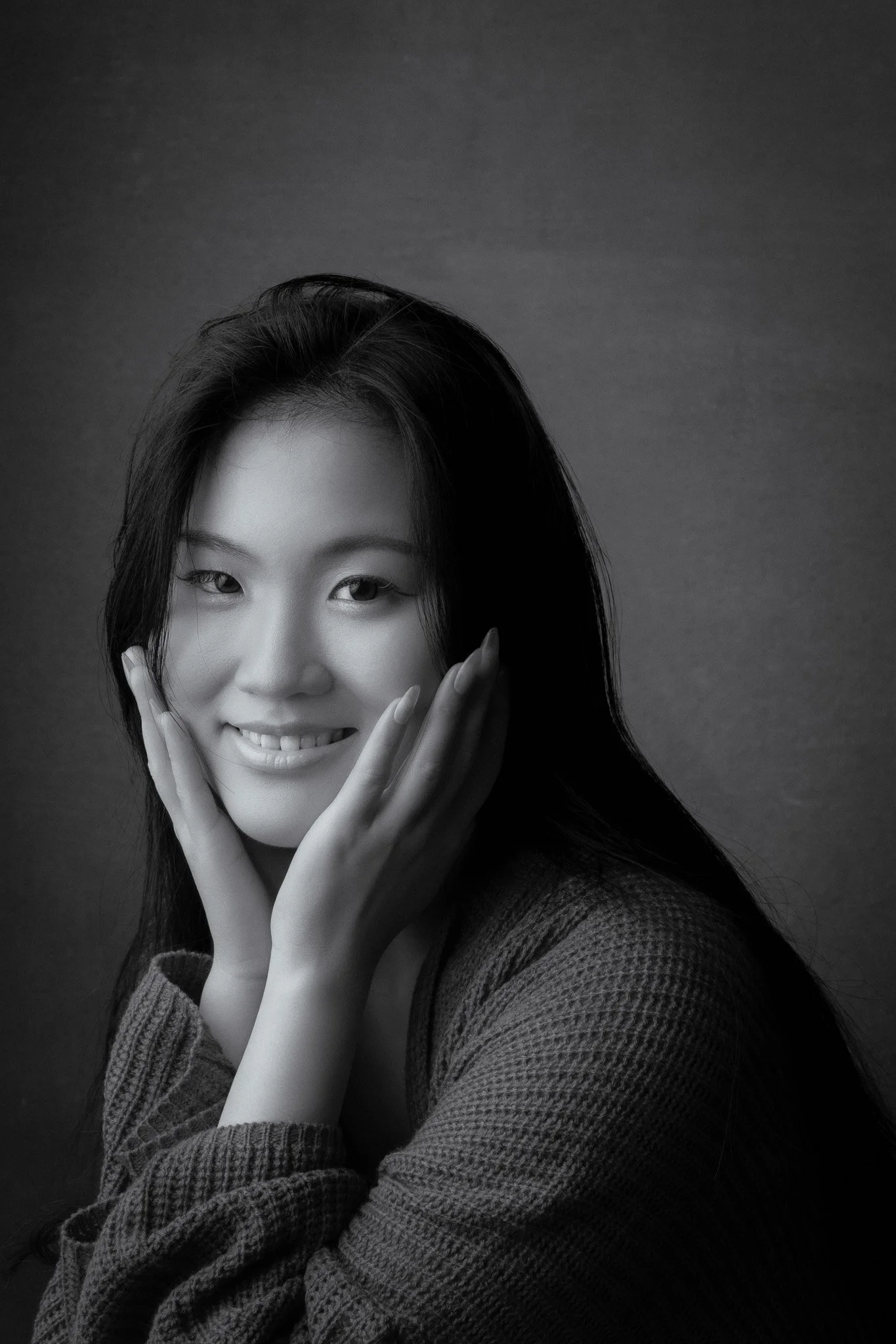 Lifestyle portrait of a young woman cradling her face with her hands and smiling at the camera
