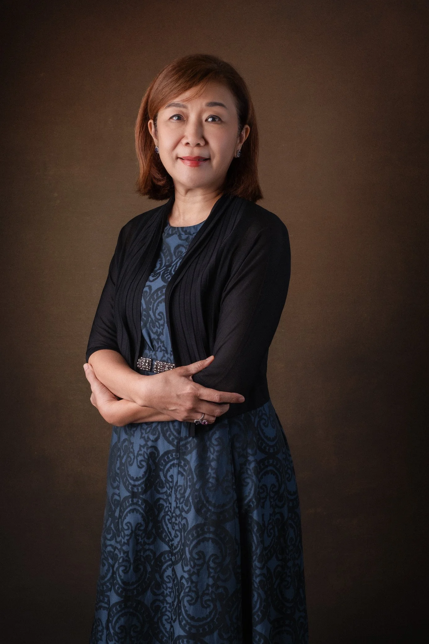 Portrait for Tan Su May, legal professional. She is standing in front of a dark background with arms in front of her. 