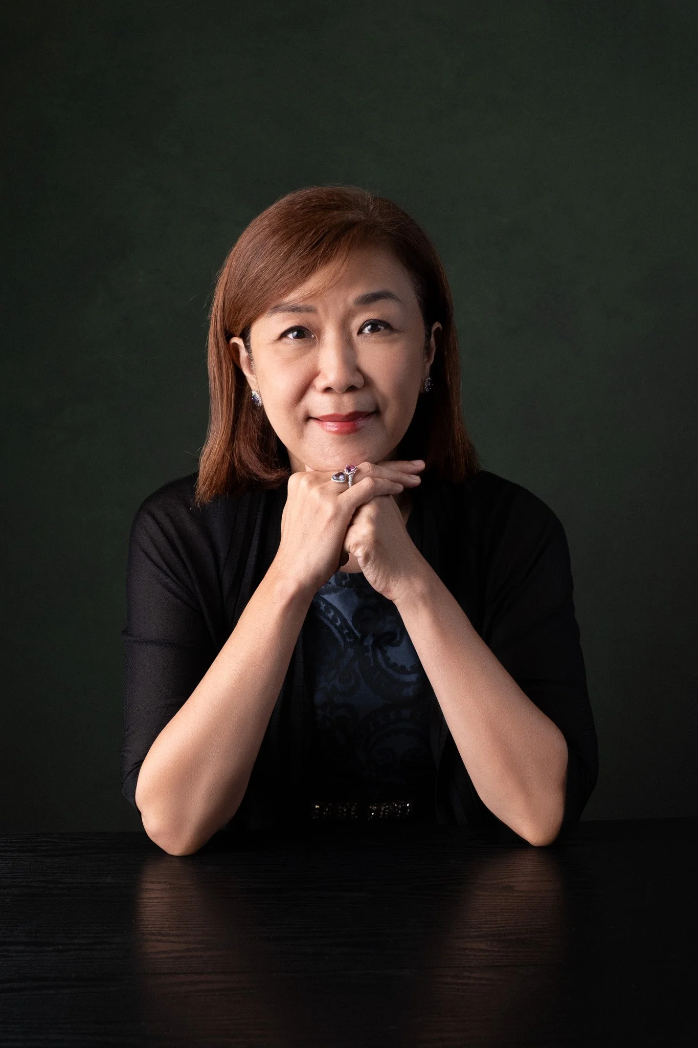 Corporate headshot for legal professional, Tan Su May. She is seated, smiling at the camera with hands below her chin. 