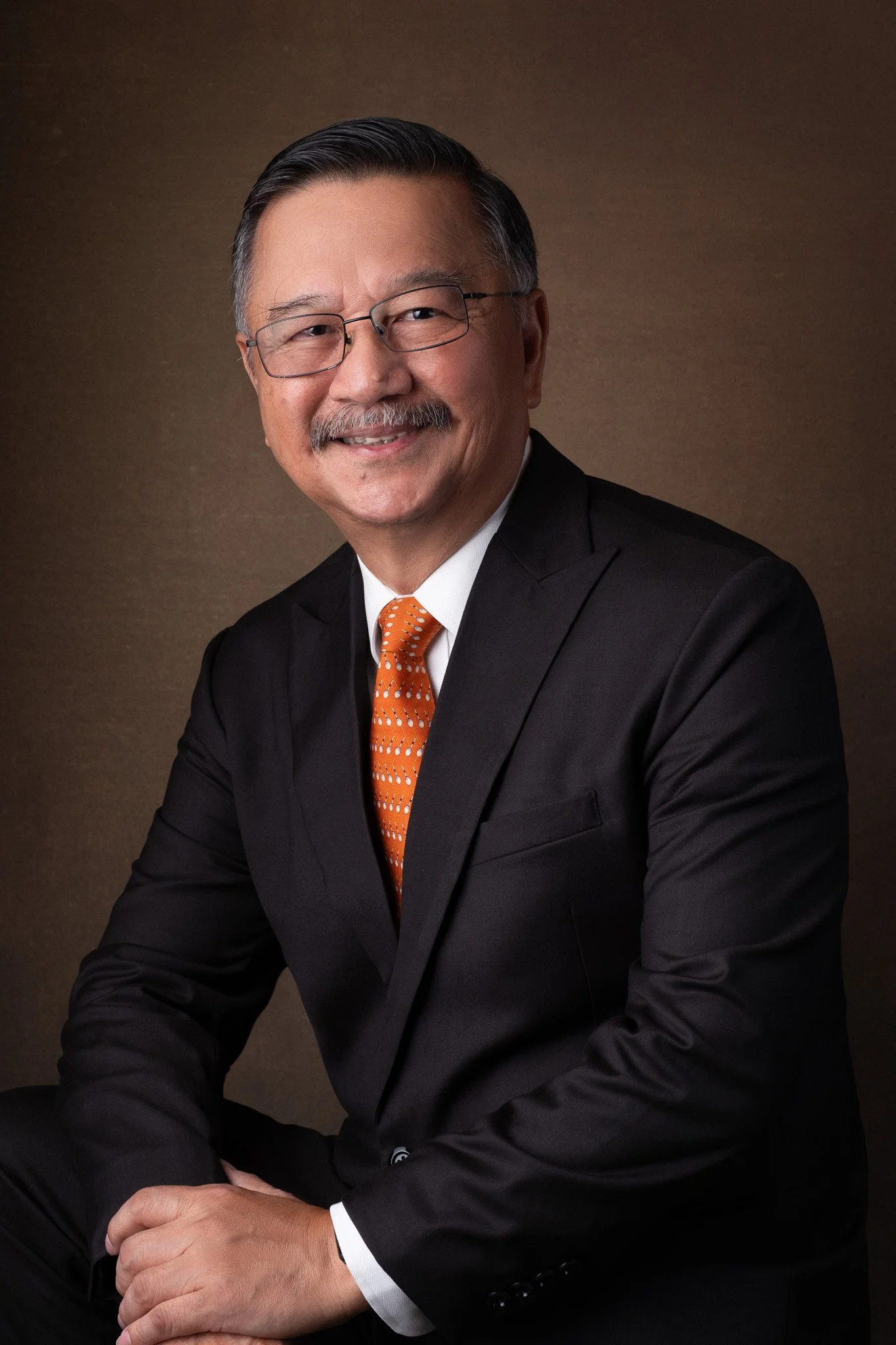Executive portrait for Teo Cheow Tong, seated and smiling. Orange tie and black blazer. Board of Committee member for Assumption English School, Singapore.