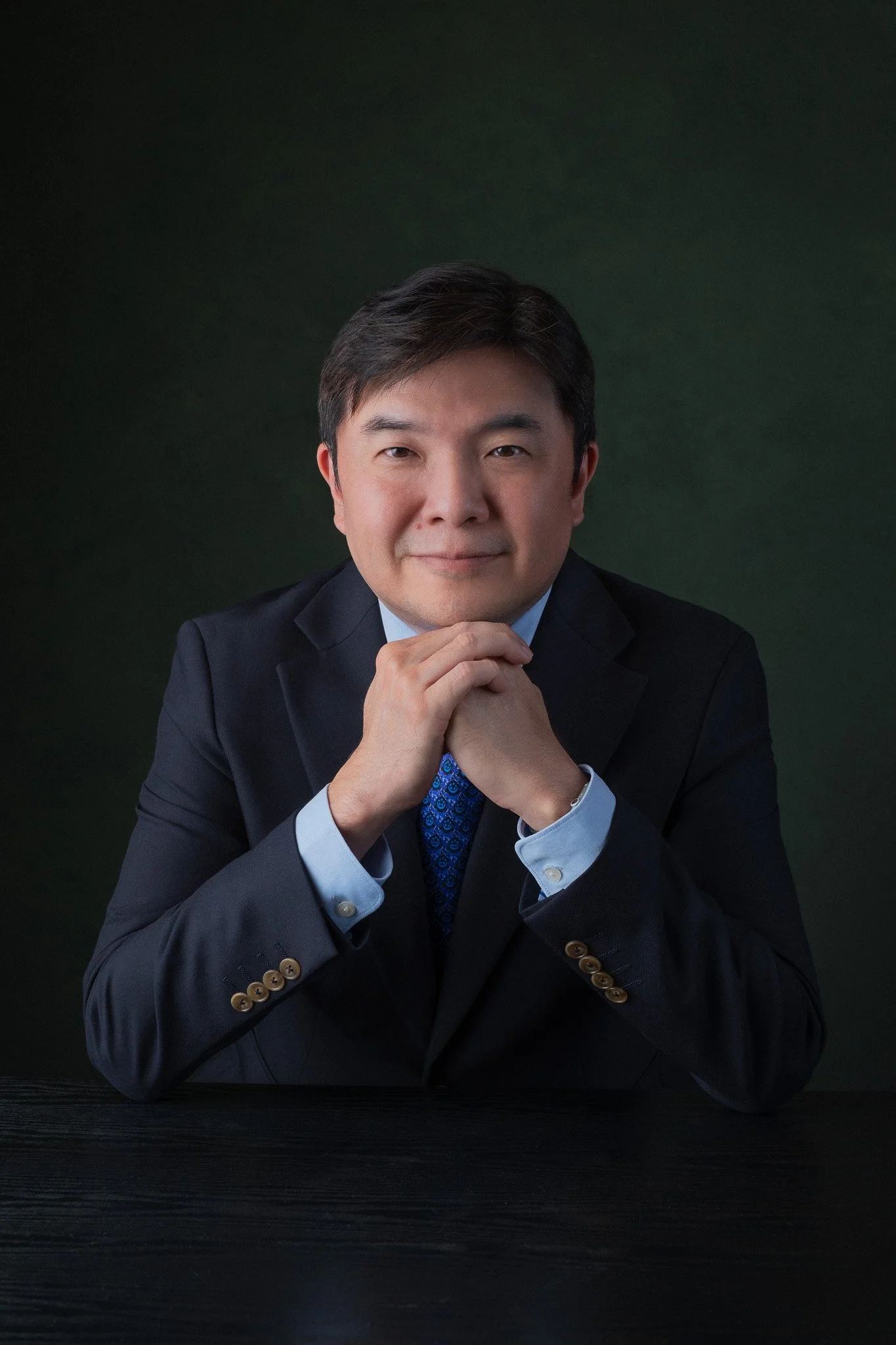 Executive portrait for Vincent Toh, principal of Assumption English School. He is seated with his hands below his chin. 