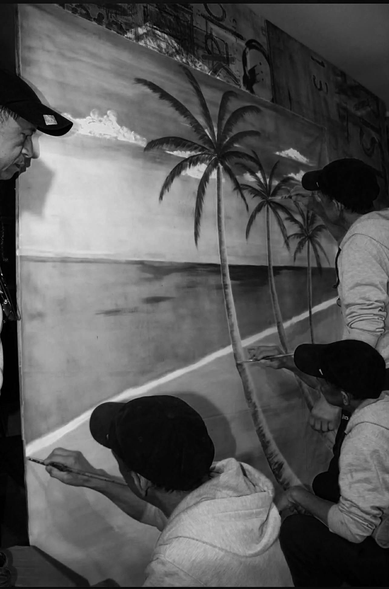 A group of people working on a painting of a beach scene with palm trees, ocean, and clouds.