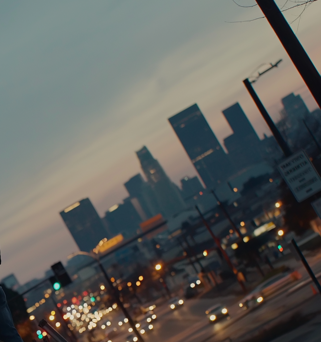City skyline during evening with skyscrapers in the background, blurred traffic in the foreground, and a cloudy sky.