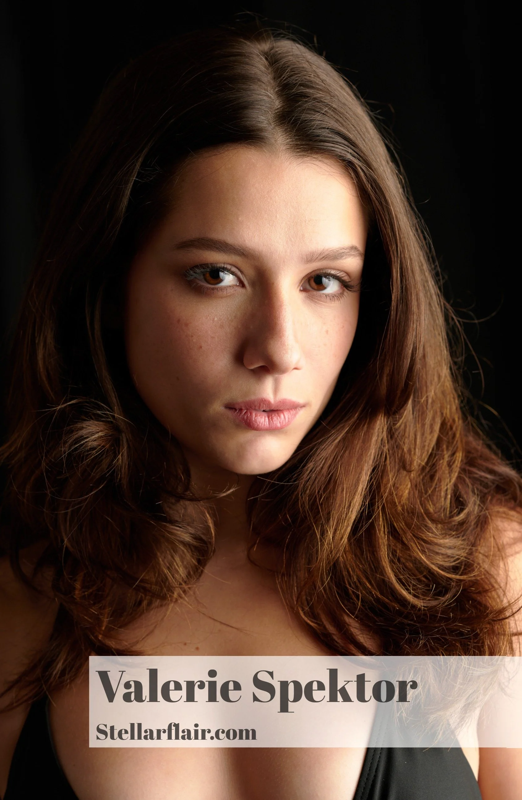 A portrait of a woman with long wavy brown hair, light skin, and brown eyes, wearing a black top with a scoop neckline, with a black background. There is a text overlay with the name 'Valerie Spektor' and the website 'Stellarfair.com'.