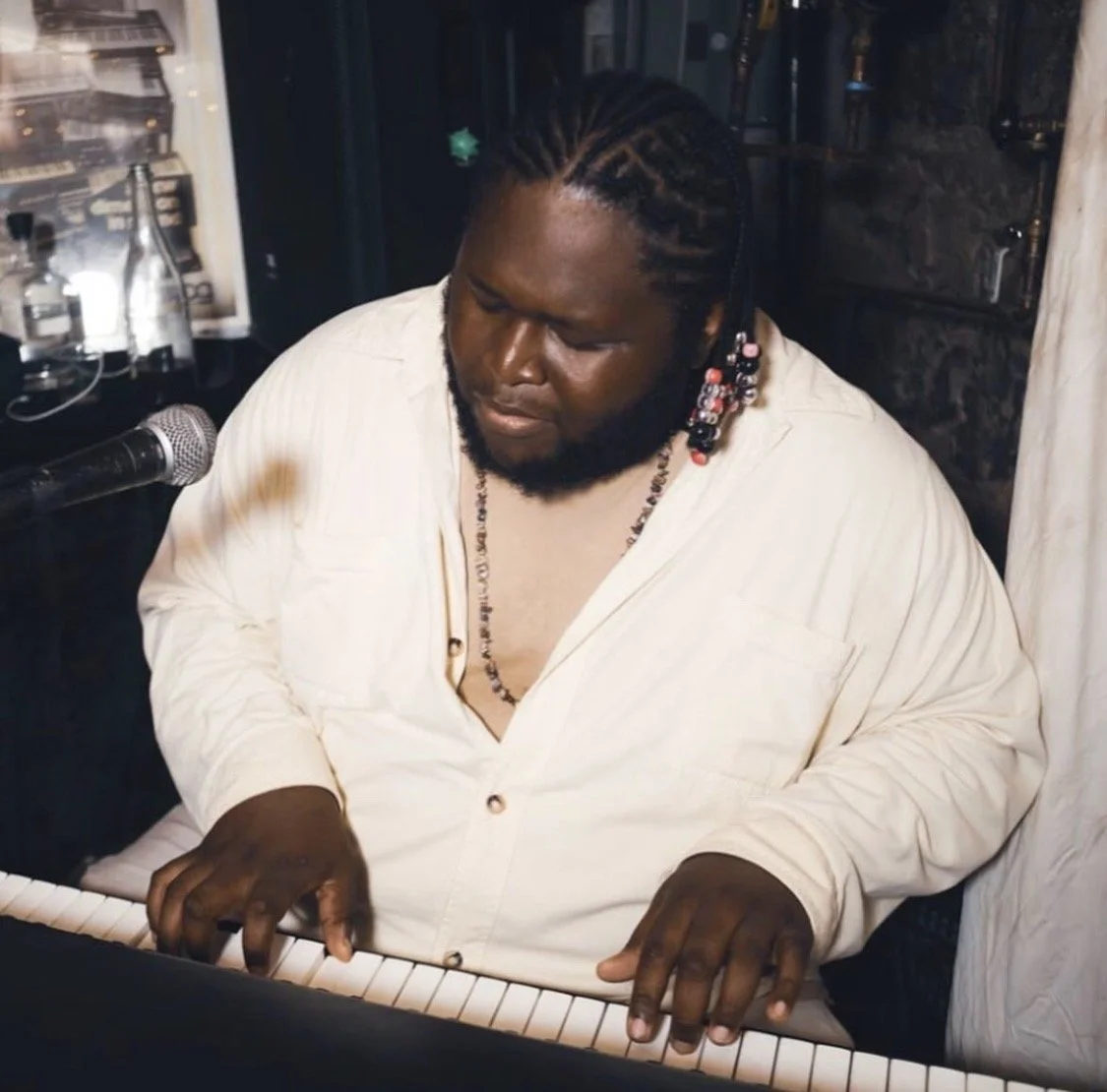 A man with braided hair and a beard playing a keyboard.