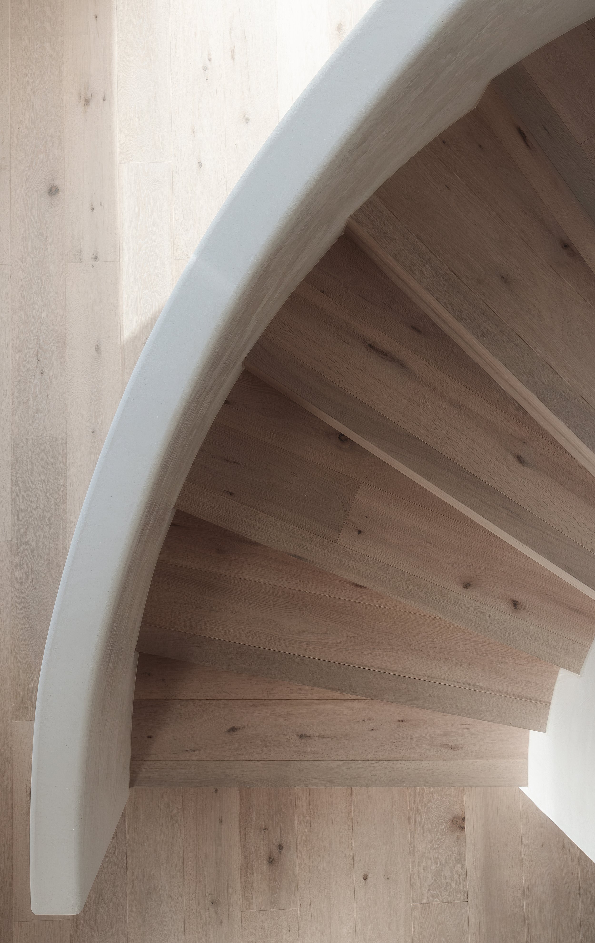 Top-down view of a curved staircase with wooden steps and a light-colored curved railing.