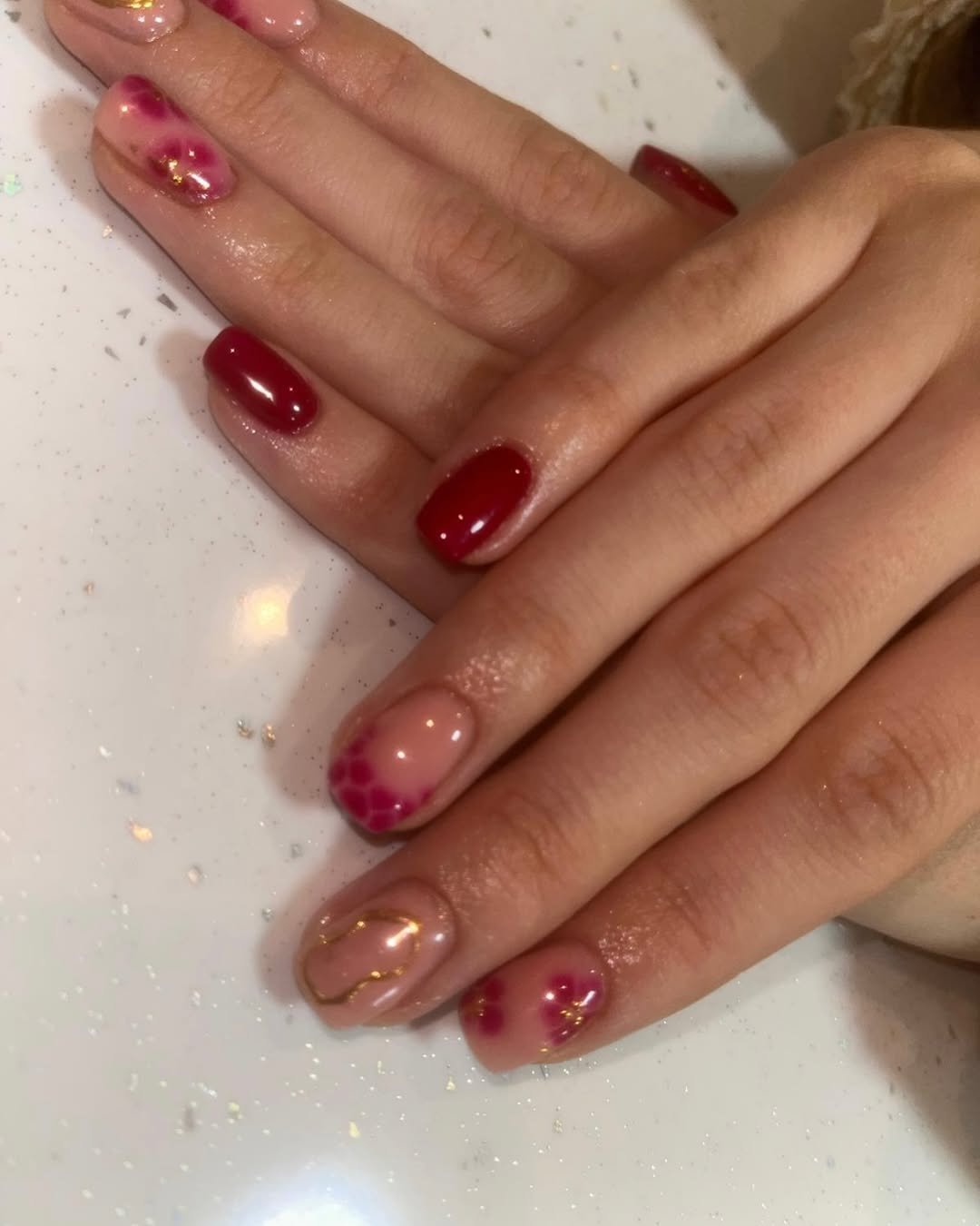 Close-up of a hand with decorated nails featuring red, pink, and gold accents.