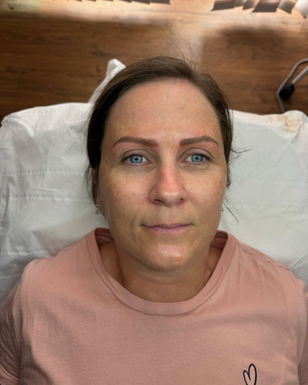 A woman with blue eyes lying on a white pillow on a wooden bed, looking directly at the camera.