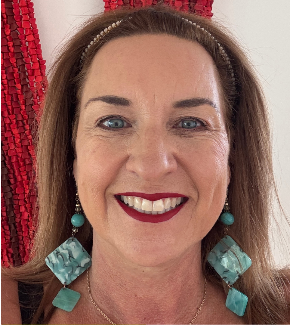 A woman with light skin, blue eyes, and long brown hair, smiling at the camera, wearing a pearl headband and large turquoise earrings, with a red textured background.