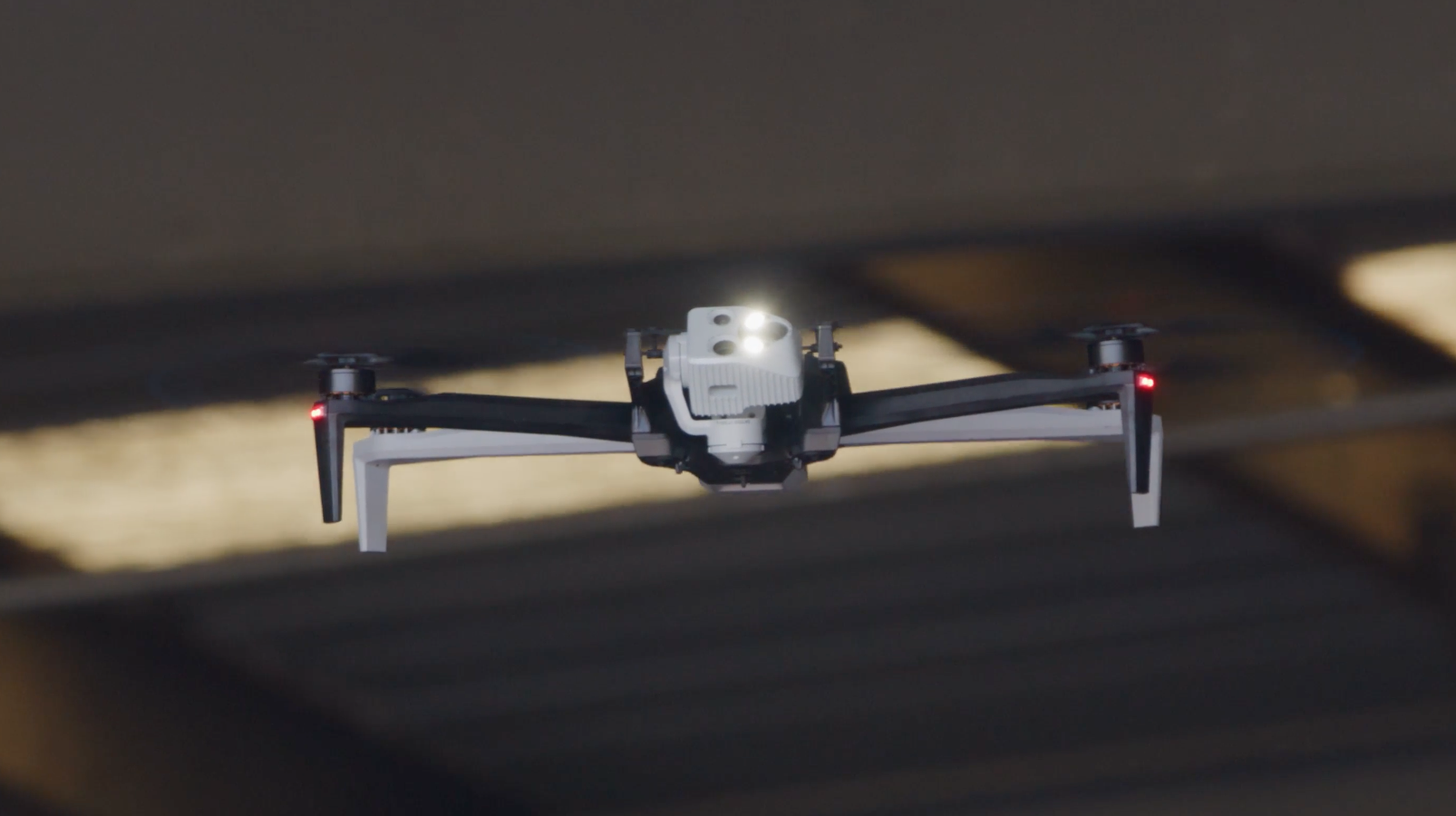A drone is flying through a space with dark beams or slats overhead.
