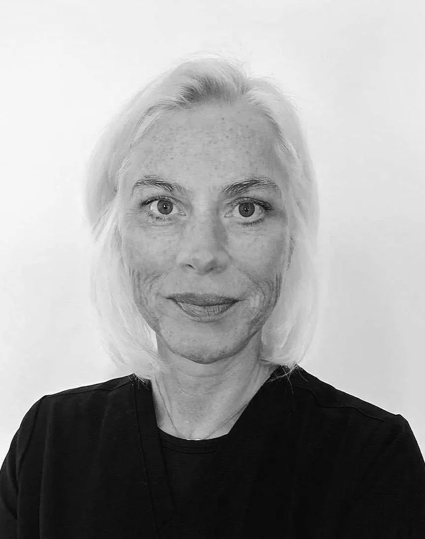 Schwarz-weiß-Foto einer älteren Frau mit blonden Haaren, die direkt in die Kamera schaut und ein schwarzes Shirt trägt.