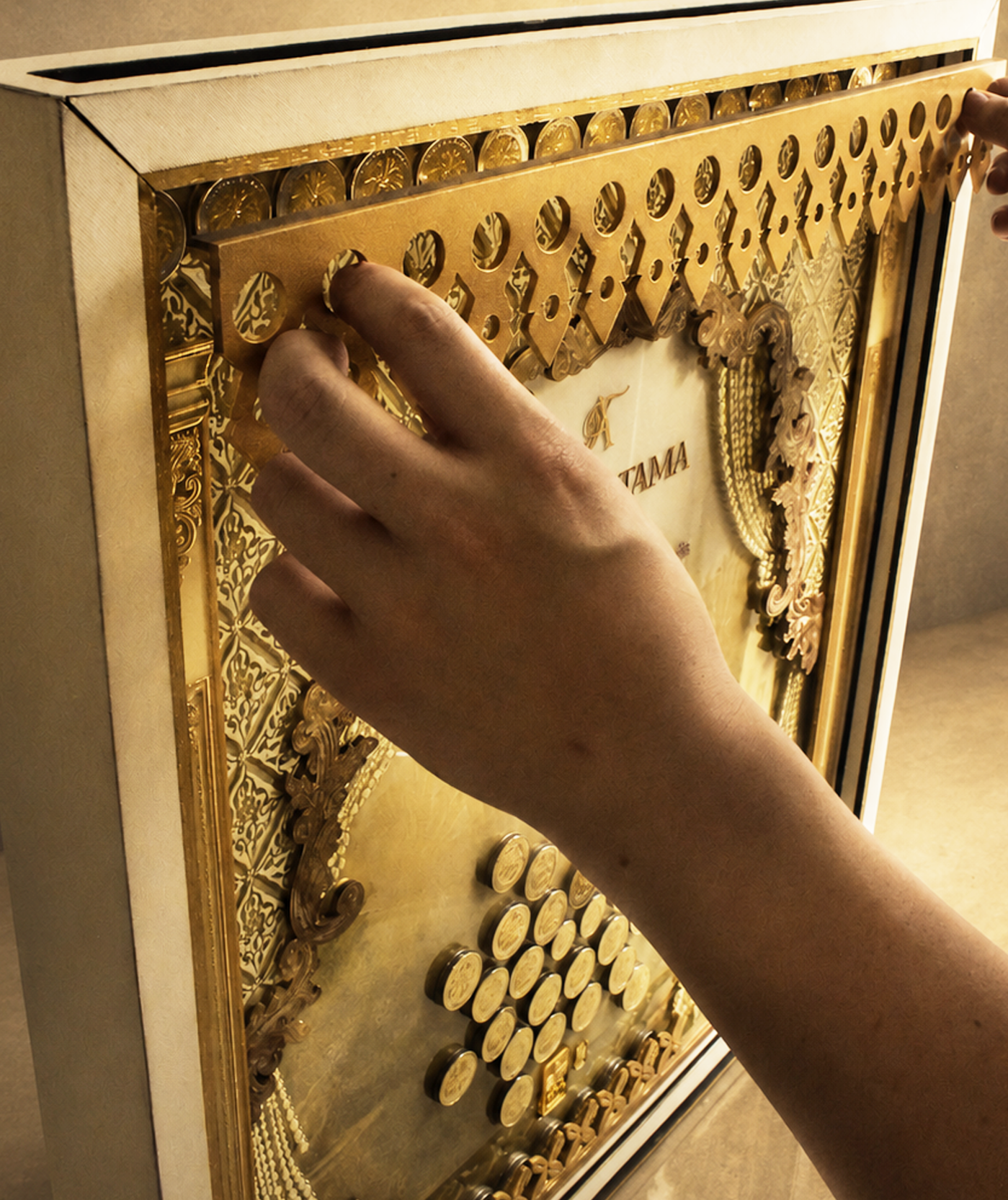 Person's hand adjusting a golden, ornate piece of an intricate, decorative object with various small circular components, possibly a clock or display case.