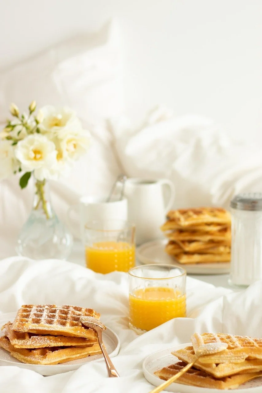 Frühstückstisch mit Waffeln, Orangensaft, Milch und Blumen