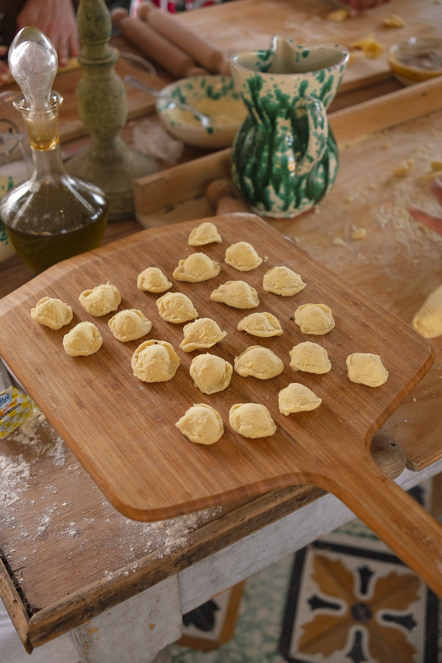 Uncut pasta dough formed into small portions on a wooden cutting board in a kitchen setting.