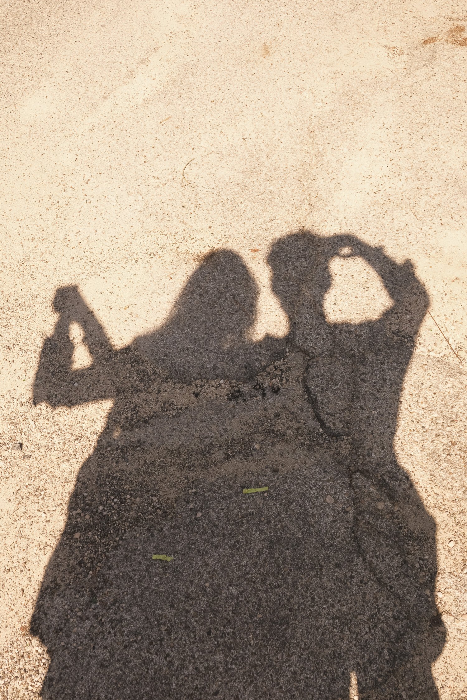 Shadow of two people making heart shapes with their hands on a sandy surface.