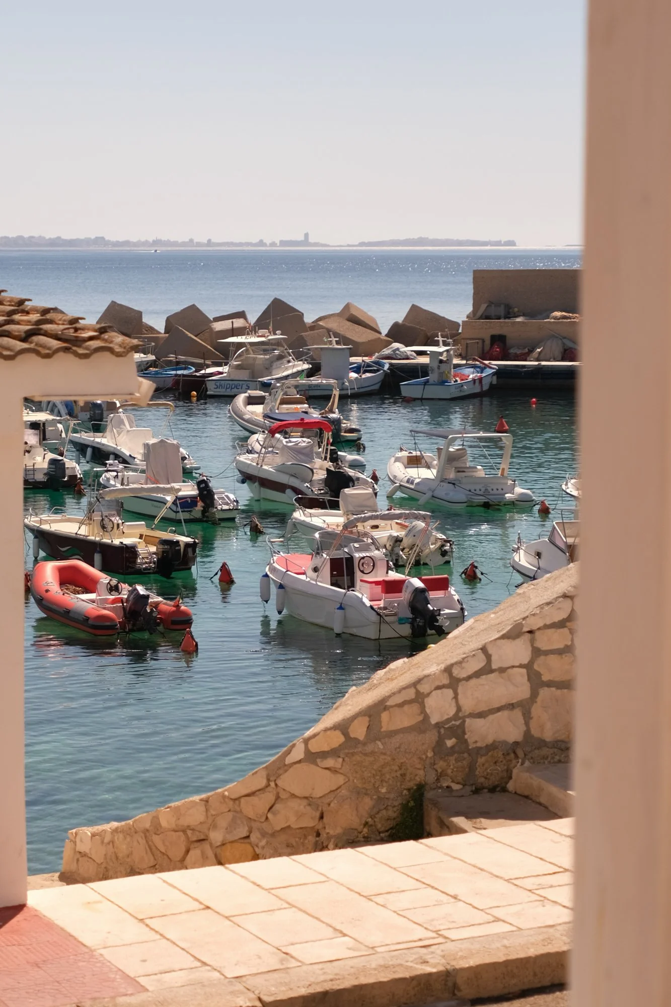 Boats docked in a marina viewed through a doorway with a stone step and a partial wall.