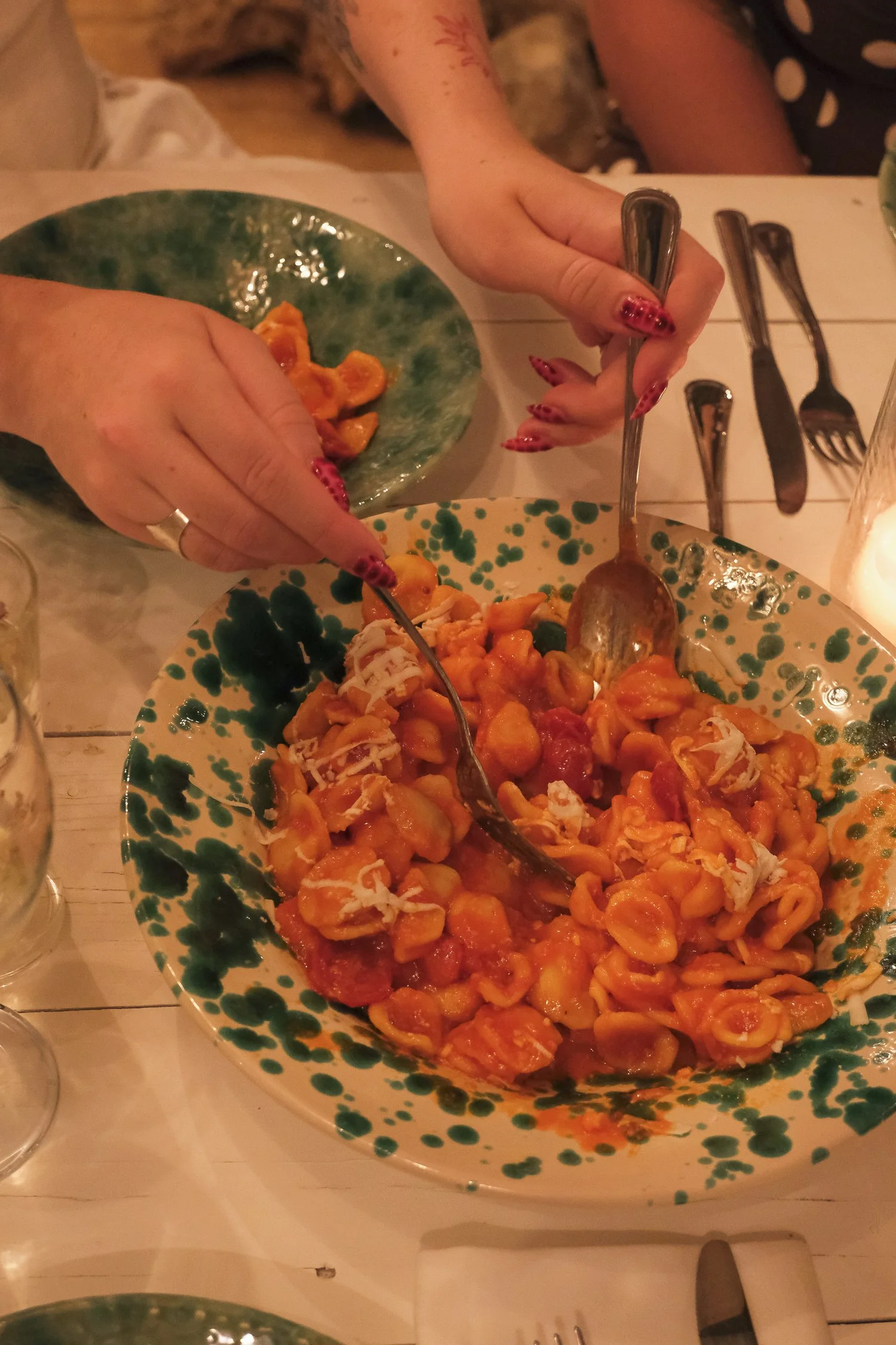 Two people sharing a bowl of pasta in a restaurant, with one person holding a fork and the other using a spoon.
