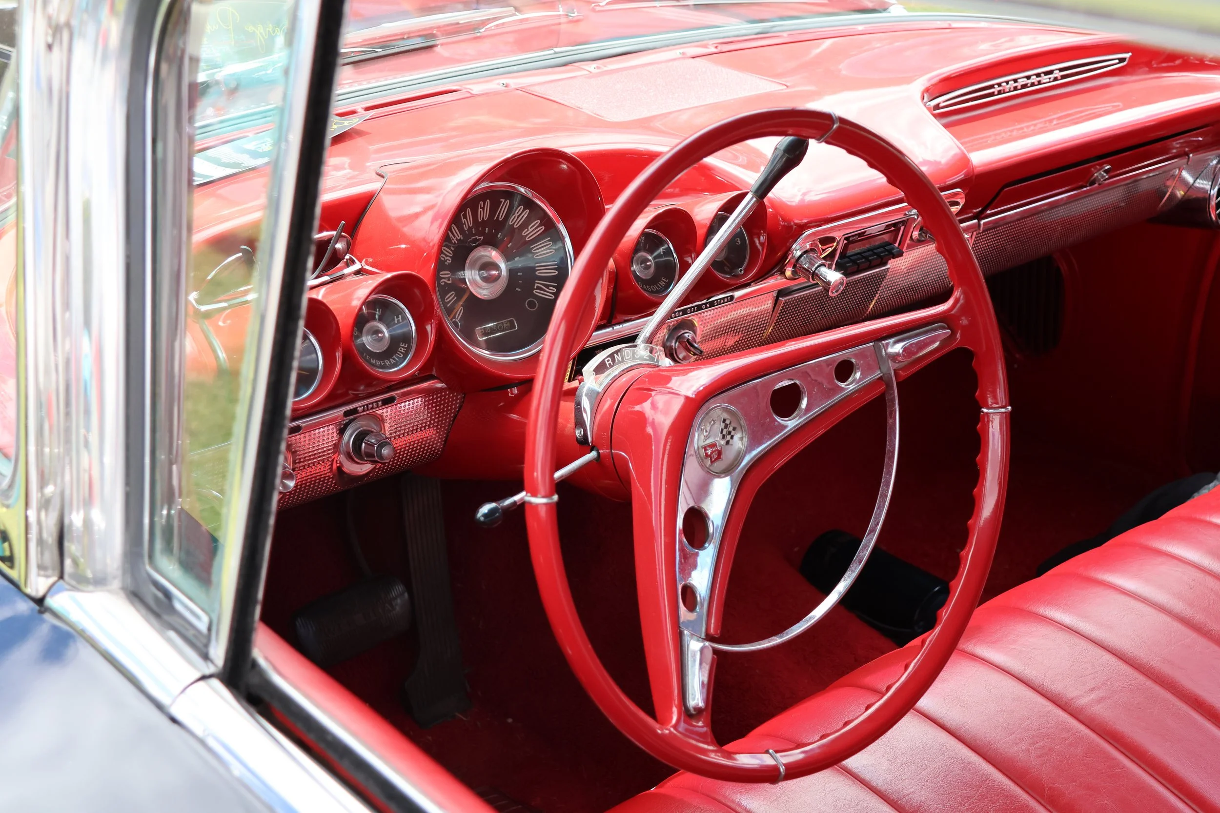 Close-up of the interior of a vintage red car, showing the steering wheel, dashboard, and gauges.