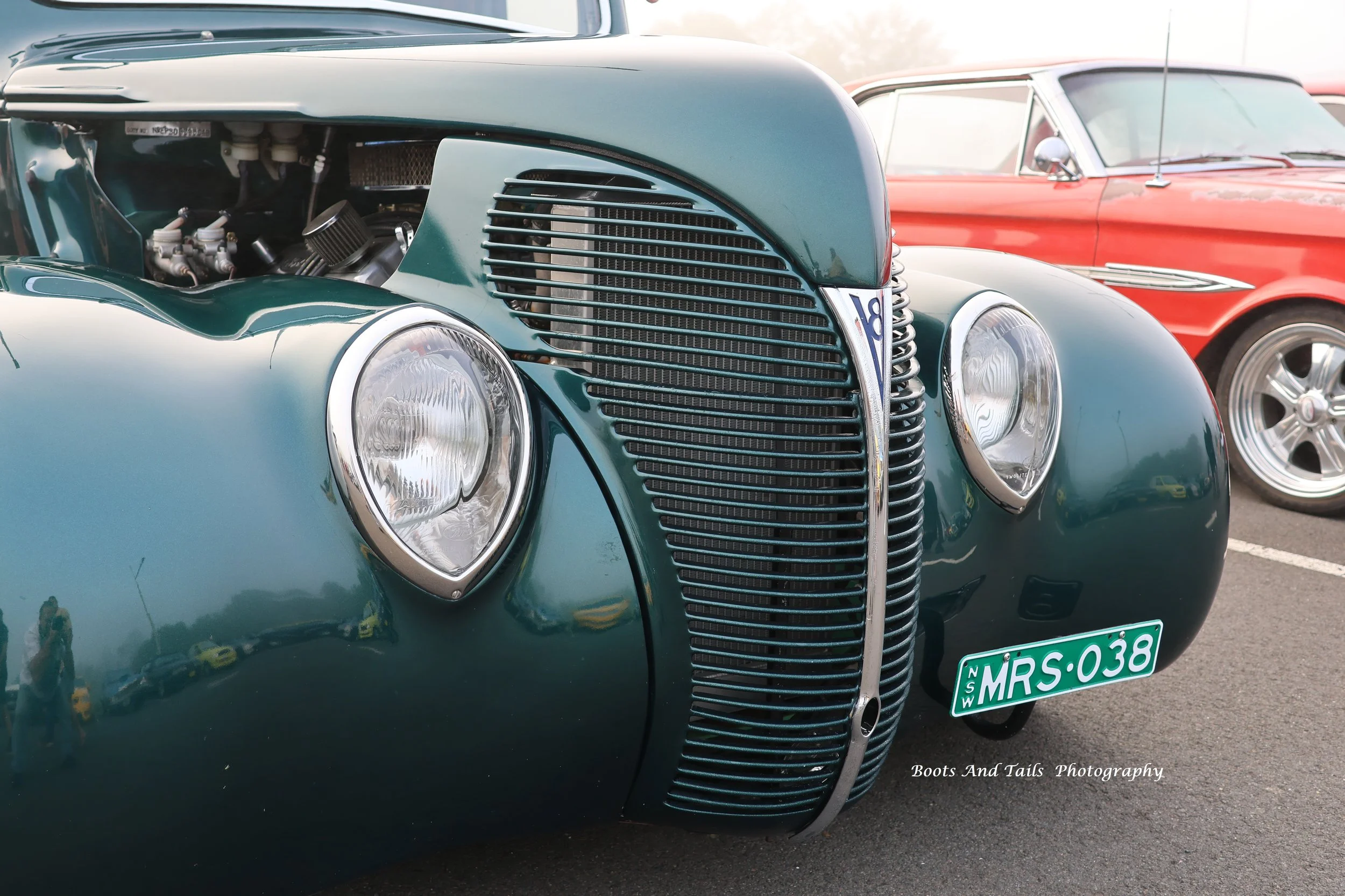 Front view of a vintage green car with visible engine, featuring a unique vertical grille, round headlights, 