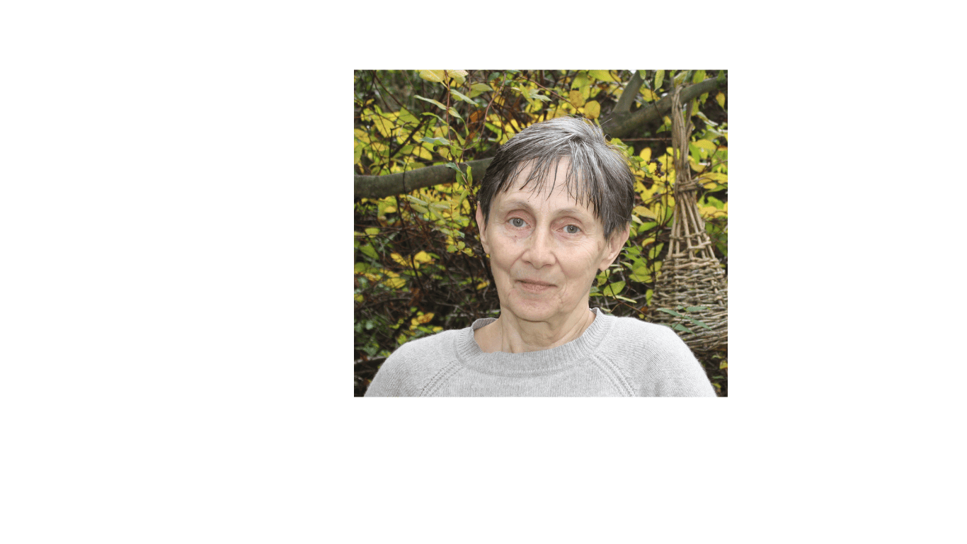 Colette Ozanne doula in a grey jumper in front of the branch of a tree in autumn with yellow leaves and a woven bird nest