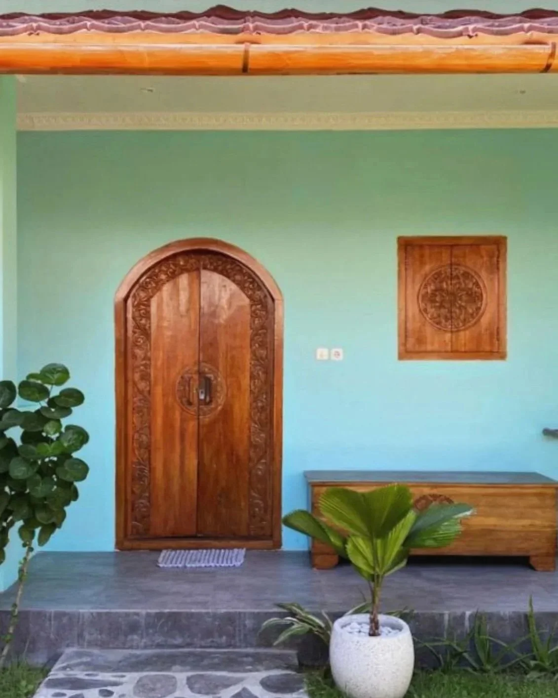 Front view of a green house with a decorative wooden door, potted plants, and wooden accents.