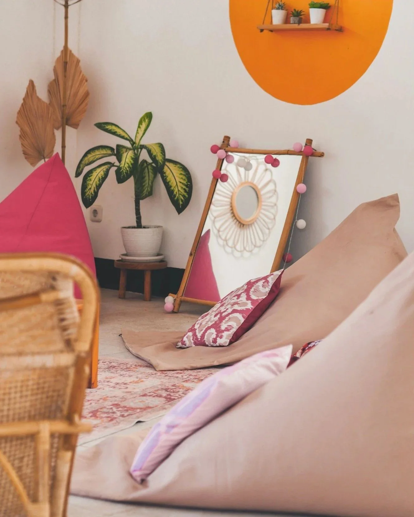 Cozy indoor space with cushions on the floor, a large leafy plant, decorative mirrors, and colorful wall accents.