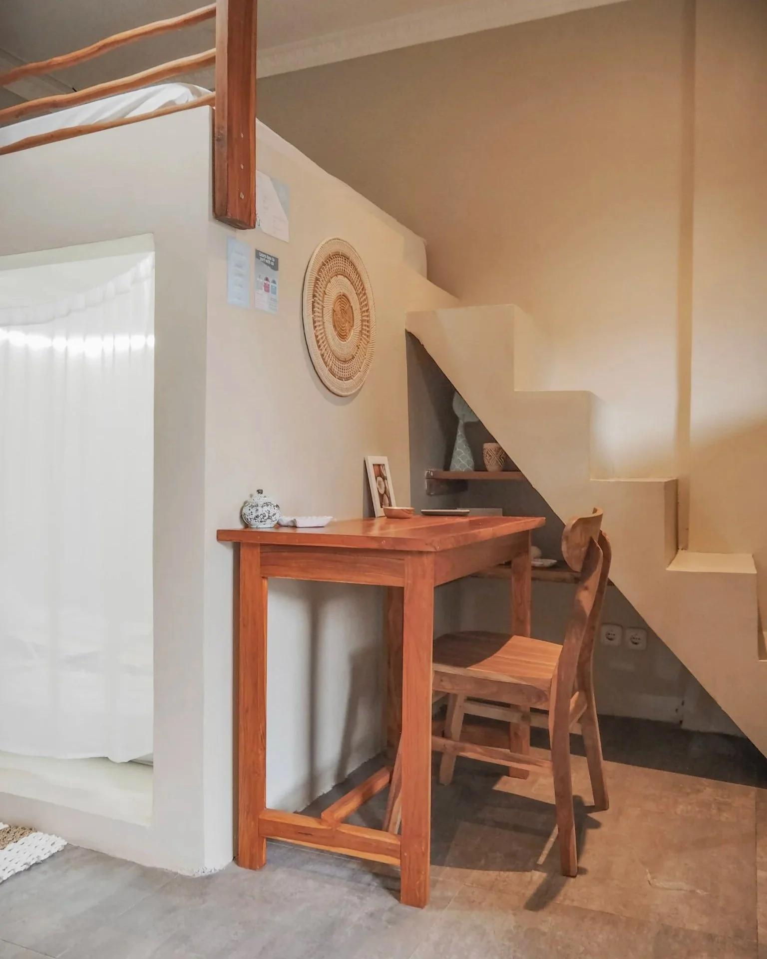 Wooden desk and chair under a staircase in a cozy room with minimal decor.