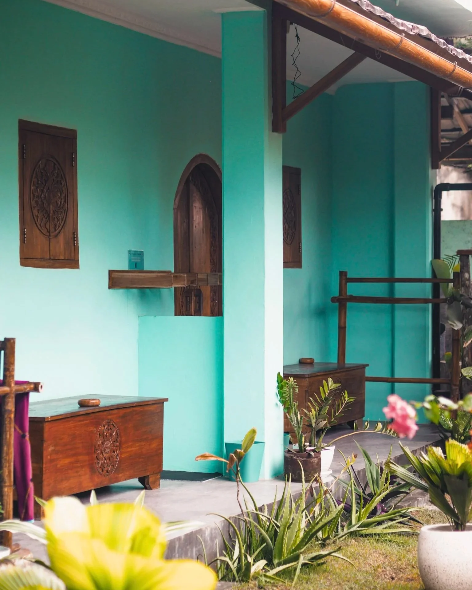 A brightly colored turquoise house with wooden shutters, a small arched wooden door, and potted plants outside in the garden.