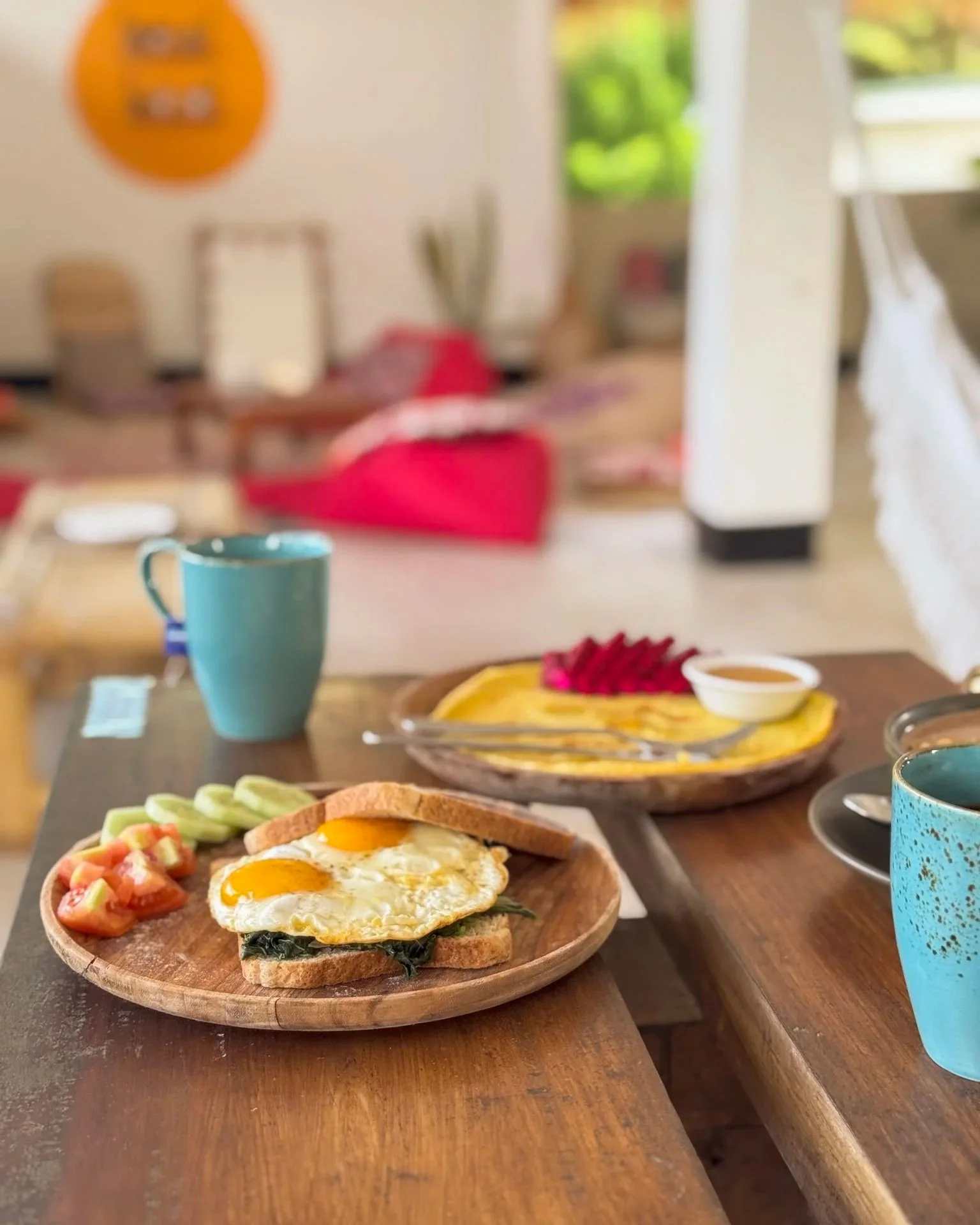 A breakfast table with a plate of eggs, toast, and vegetables, a cup, and a bowl of fruit, in a cozy kitchen setting.