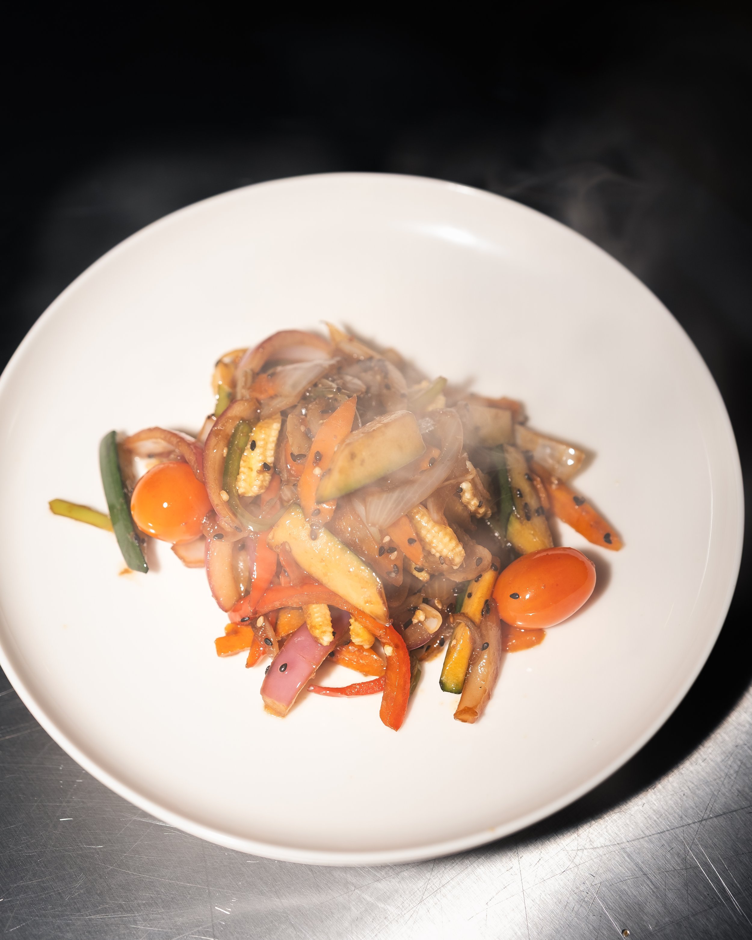Plato de verduras salteadas con tomates cherry, zanahorias, calabacín, cebolla y semillas de sésamo.