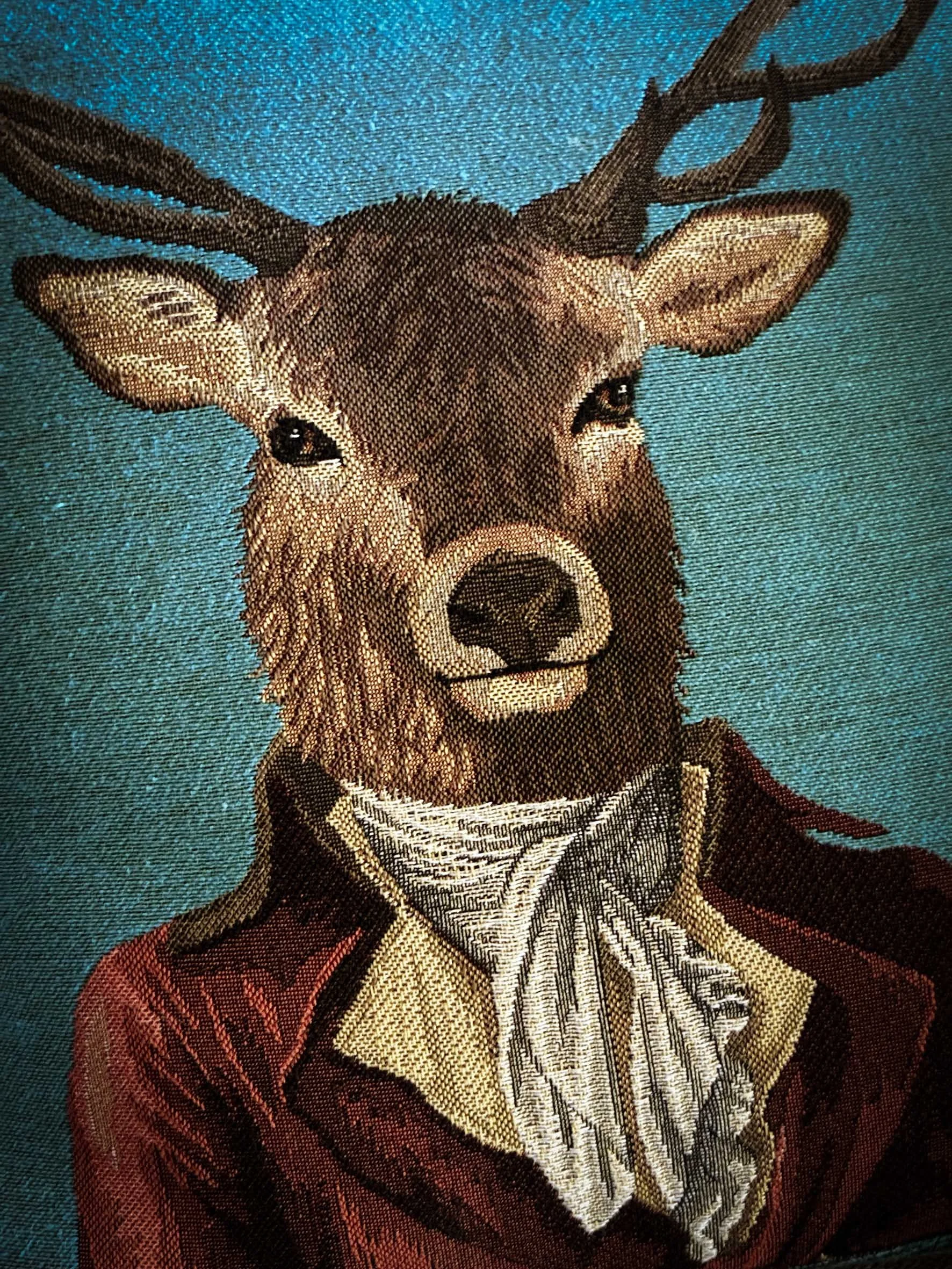 A leather tapestry in the style of embroidery or textile art depicting a sitting dog wearing a red dress and a shirt, against a blue background.