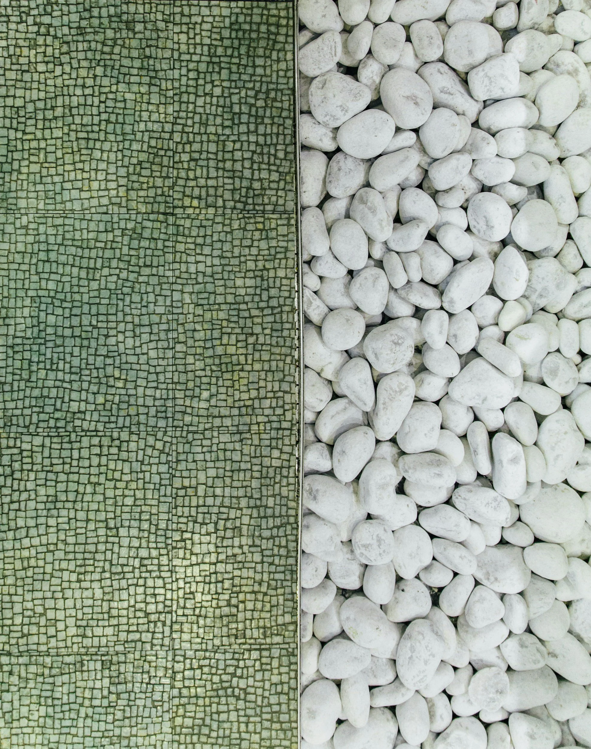 The image is divided into two sections: the left side features a mosaic of small greenish-gray cobblestones arranged in a curved pattern, while the right side displays a pile of smooth, white pebbles.