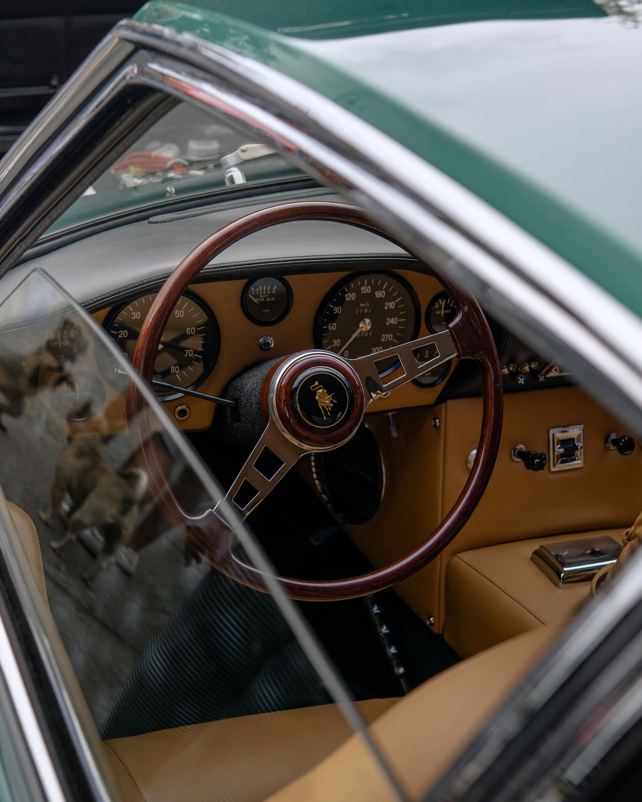 Interior view of a vintage car with a wooden steering wheel, classic dashboard gauges, beige upholstery, and a manual gear shift with a chrome handle.