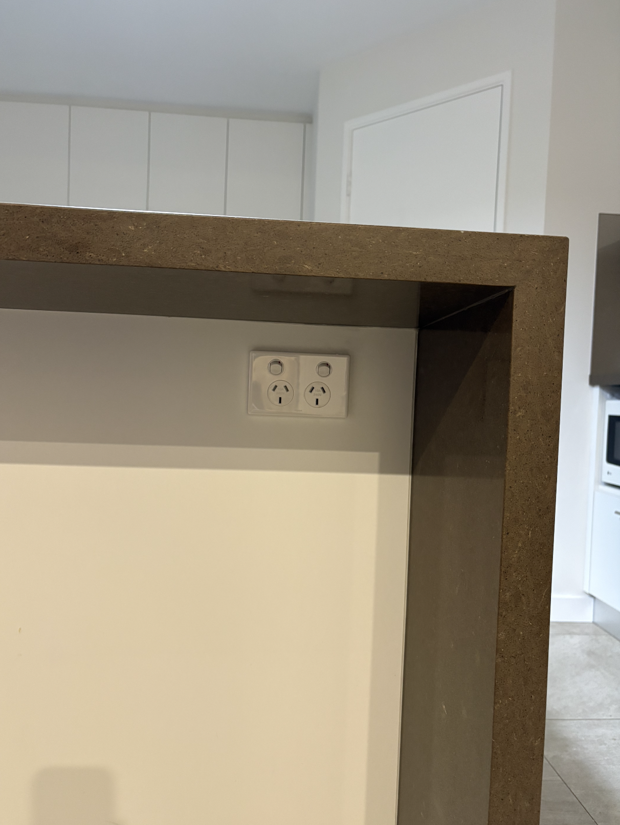 Close-up of a kitchen counter with a brown surface and a power outlet on the wall below it.