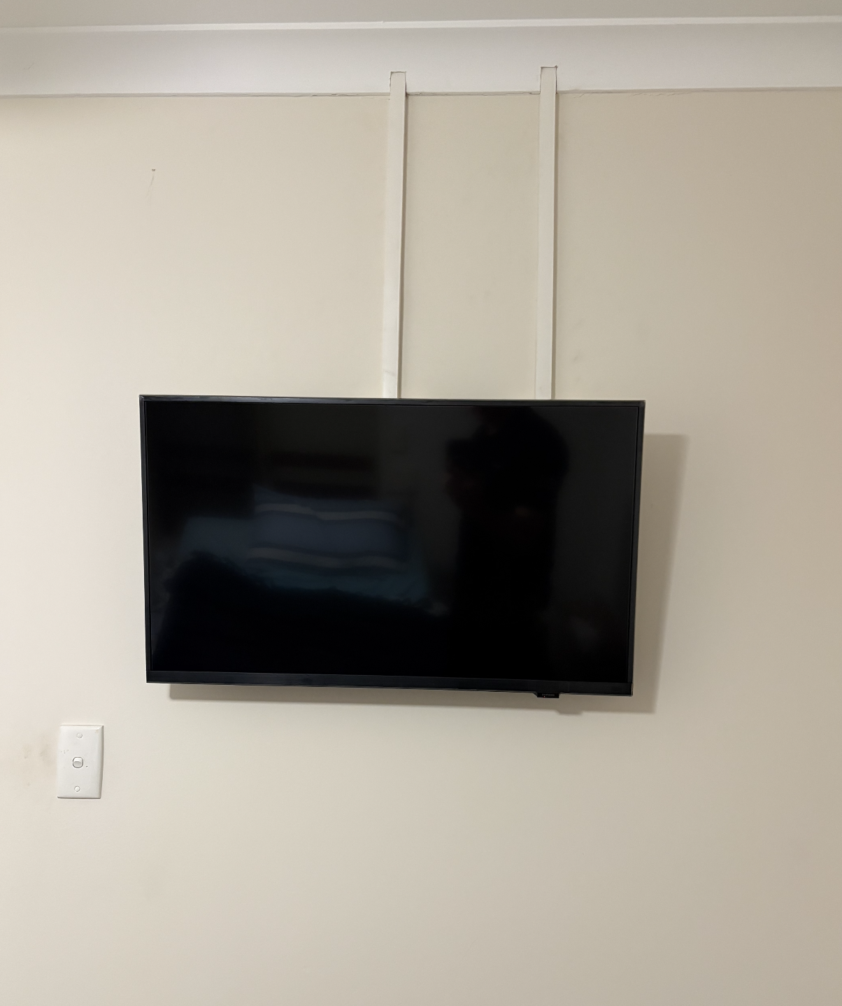 Wall-mounted flat-screen TV on a beige wall, with a white electrical outlet below it.