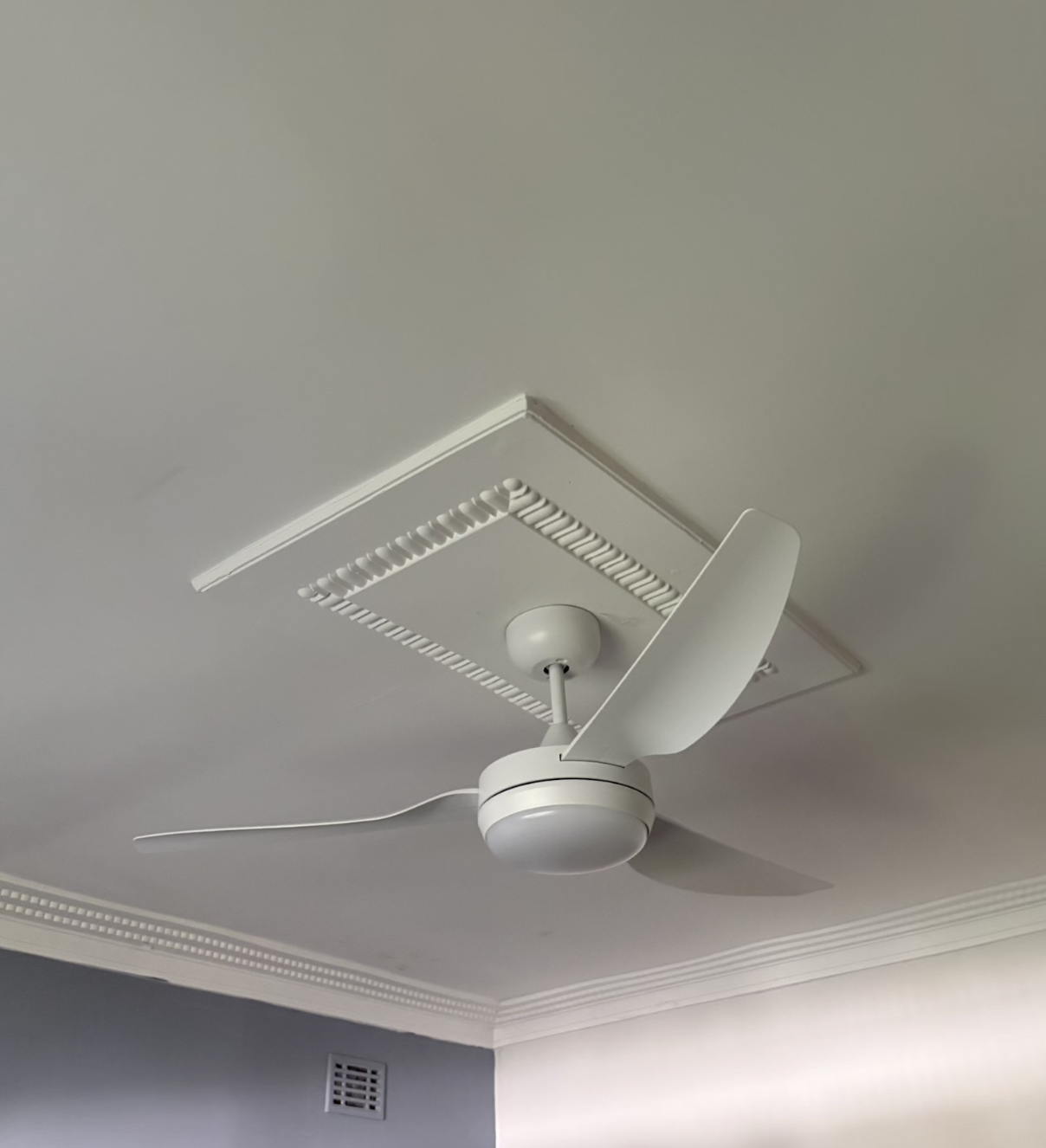 White ceiling fan with a light fixture on a white ceiling, with a rectangular vent nearby.