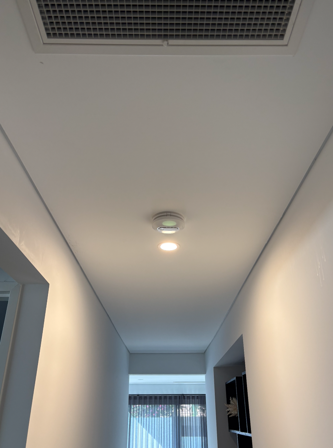 Ceiling with air vent, smoke detector, and recessed light in a modern hallway