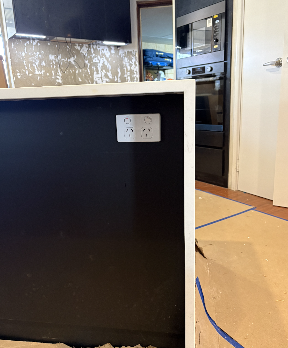 Close-up of a black and white kitchen island with electrical outlets on the side, in a kitchen with black appliances and a partially unfinished wall.