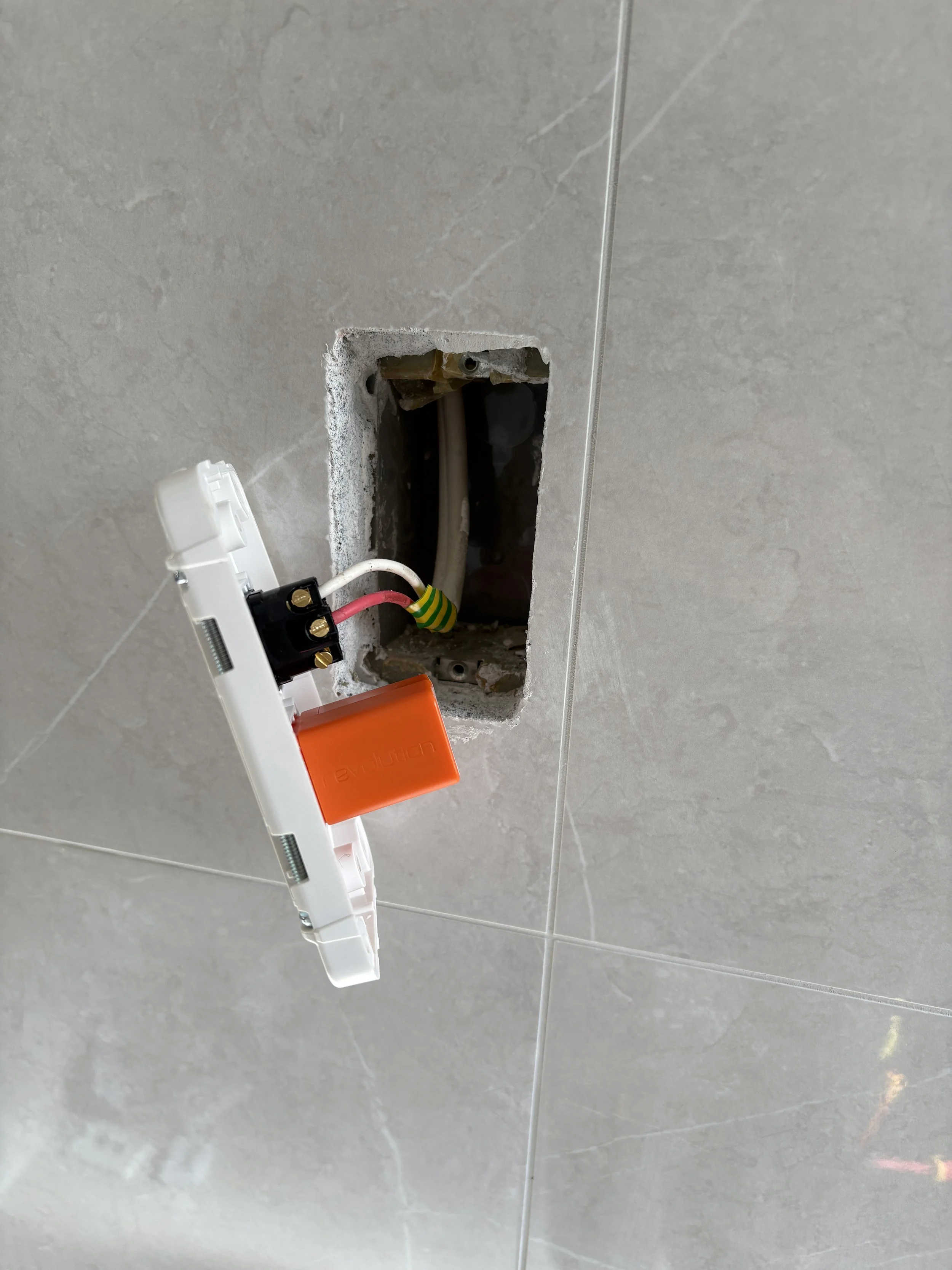 Recessed electrical box in a tiled wall with wires connected and a removed cover plate.