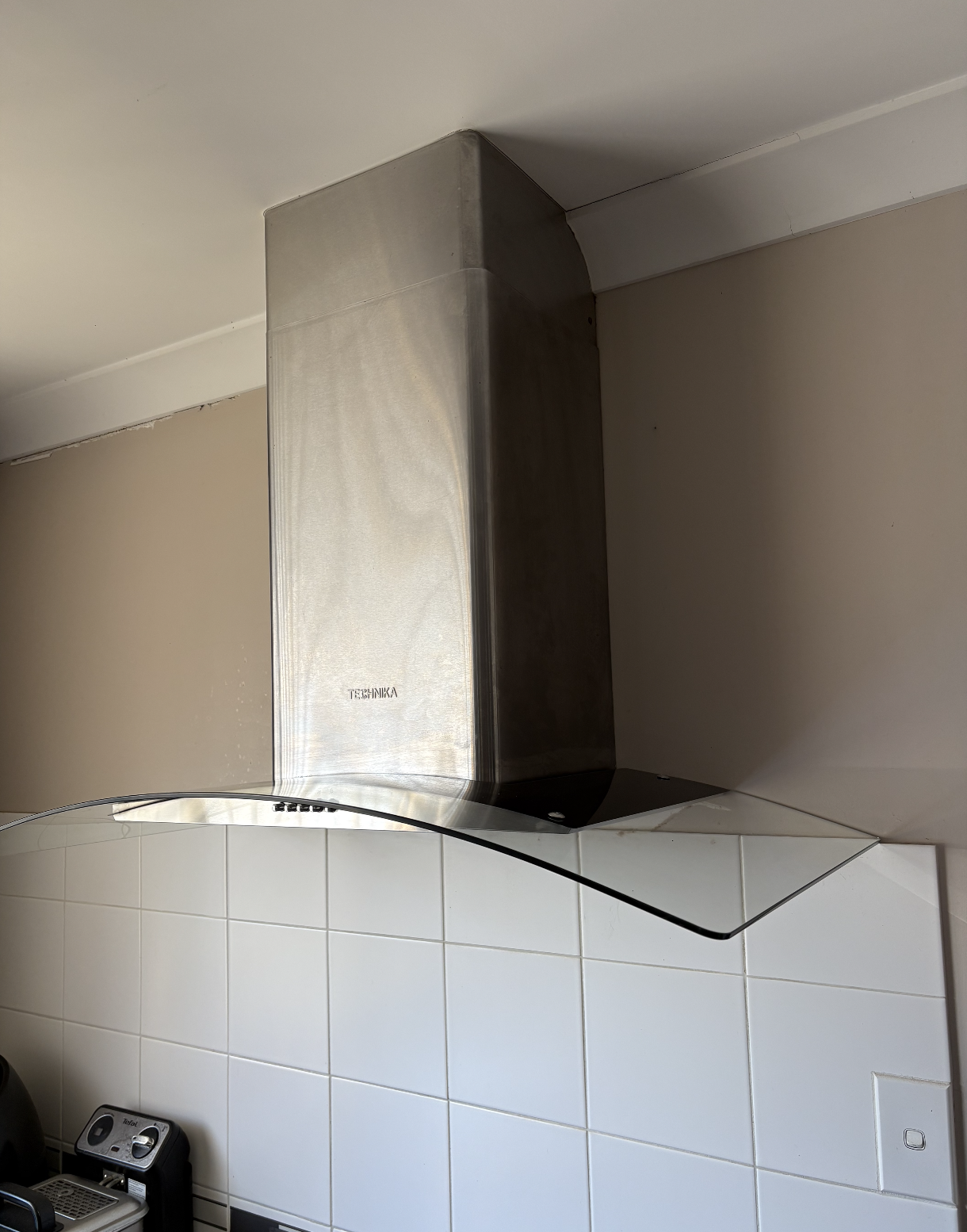 A modern kitchen with a stainless steel range hood mounted above white tiled wall.