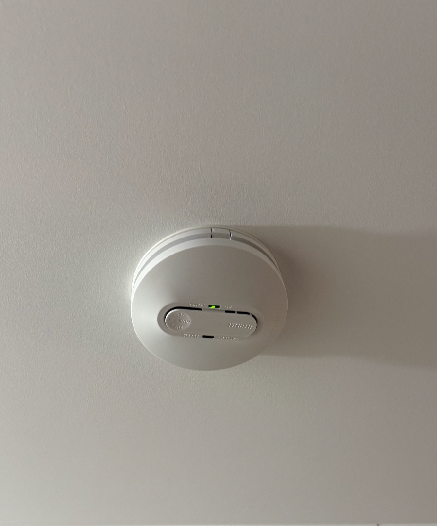 A white smoke detector mounted on a ceiling.