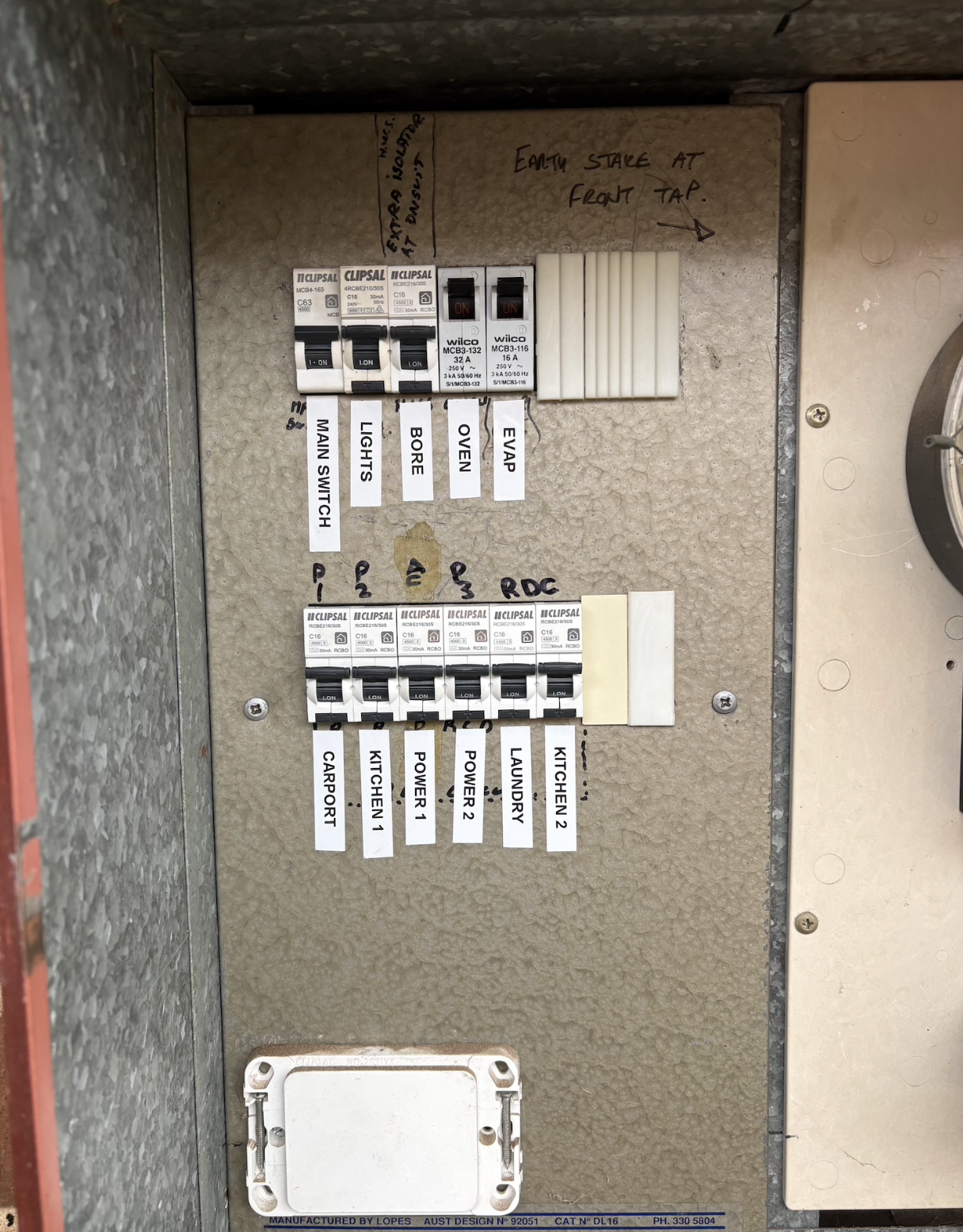 Electrical breaker panel with labeled switches for garage port, kitchen 1, power 1, power 2, laundry, kitchen 2, and other electrical components, with handwritten notes and labels.
