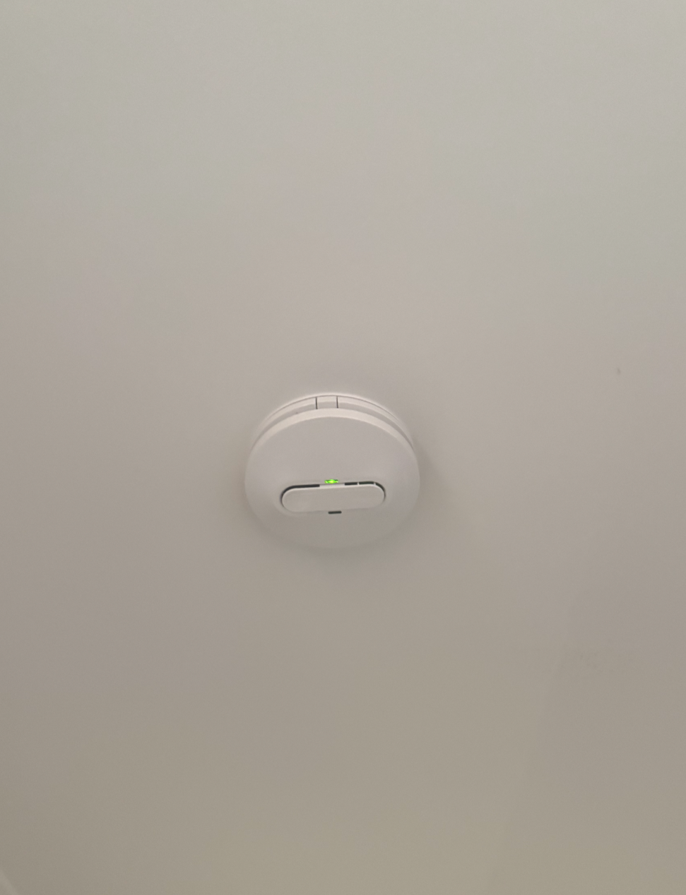 Close-up of a ceiling smoke detector with a small green light.