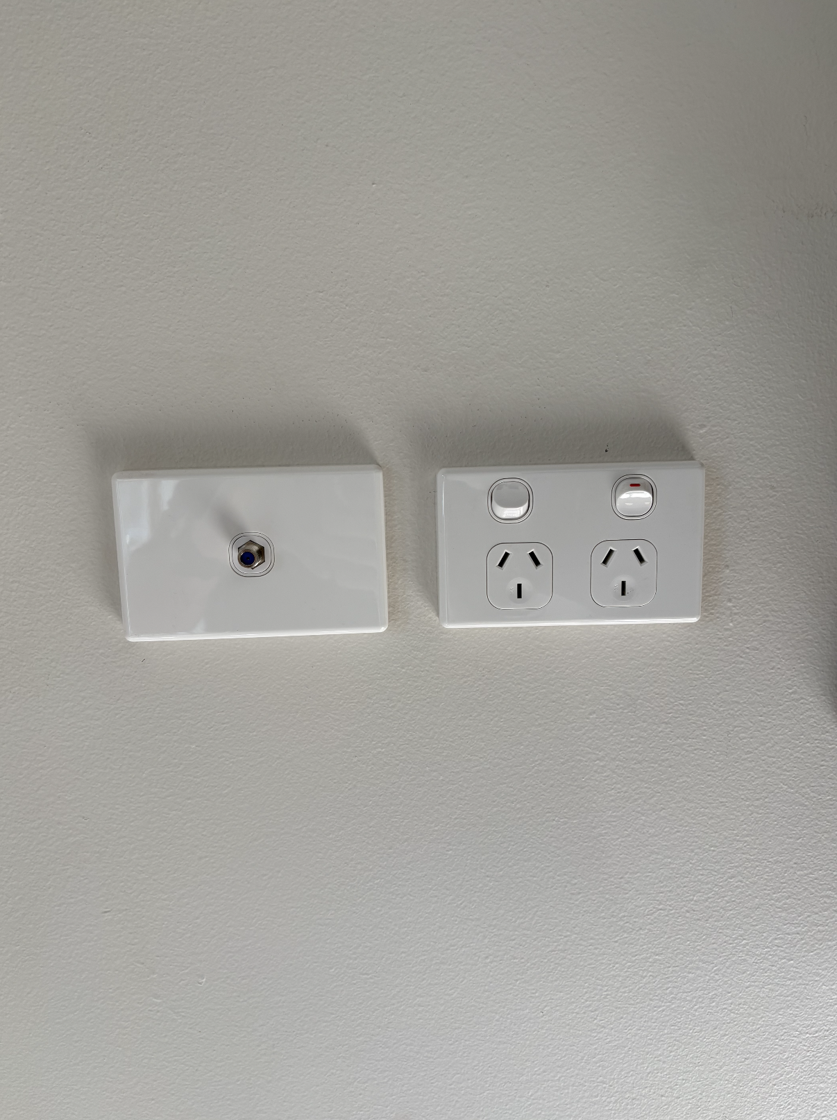 Electrical wall socket with two power outlets and a blank cover plate on a beige wall.