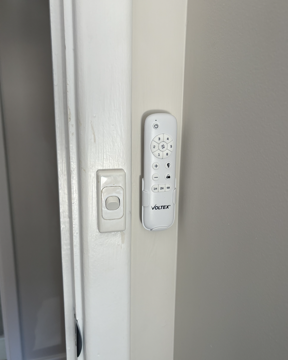 Remote control mounted on a wall next to a light switch.