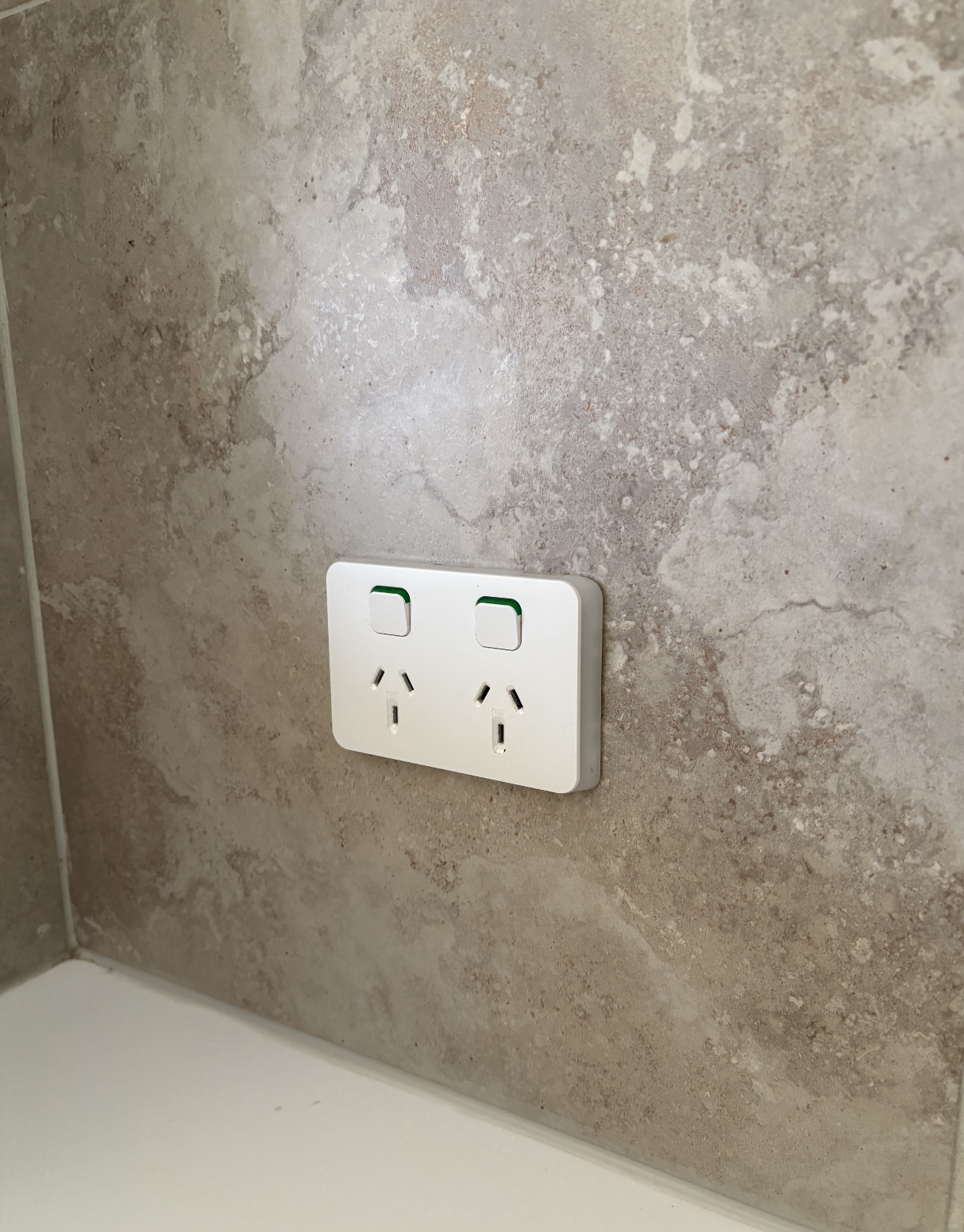 A white double power outlet with two switches on a beige stone-textured wall.