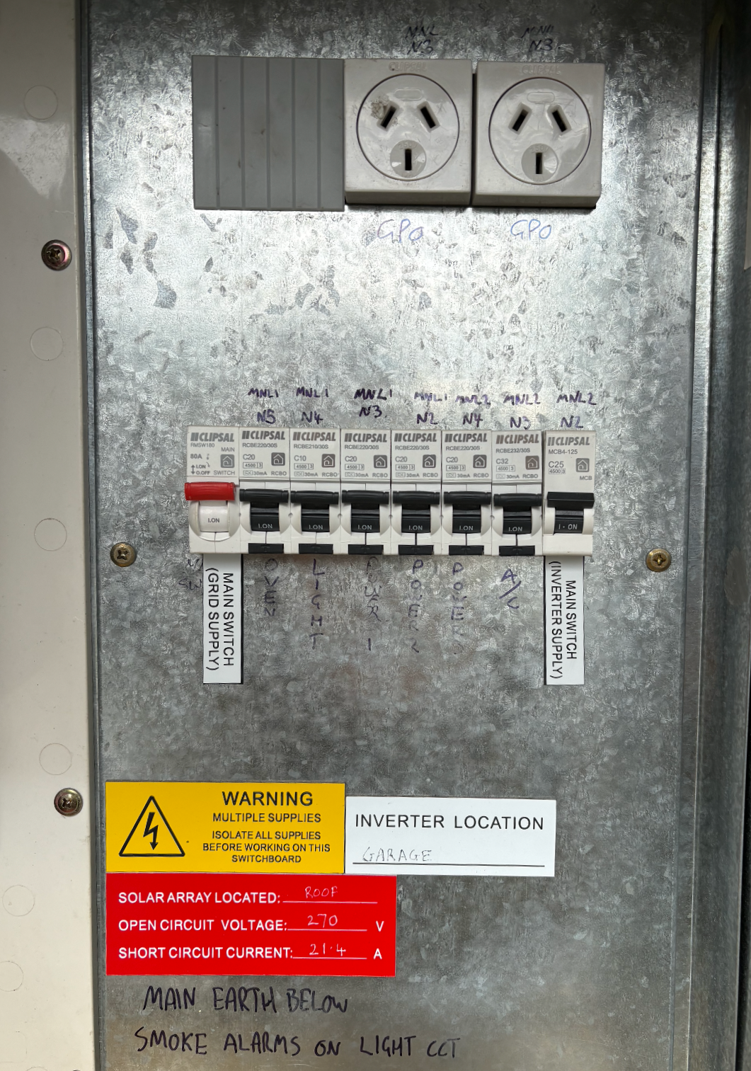Electrical circuit breaker panel with labeled switches, warning labels about solar array and circuit voltage, and handwritten notes on the metal surface.