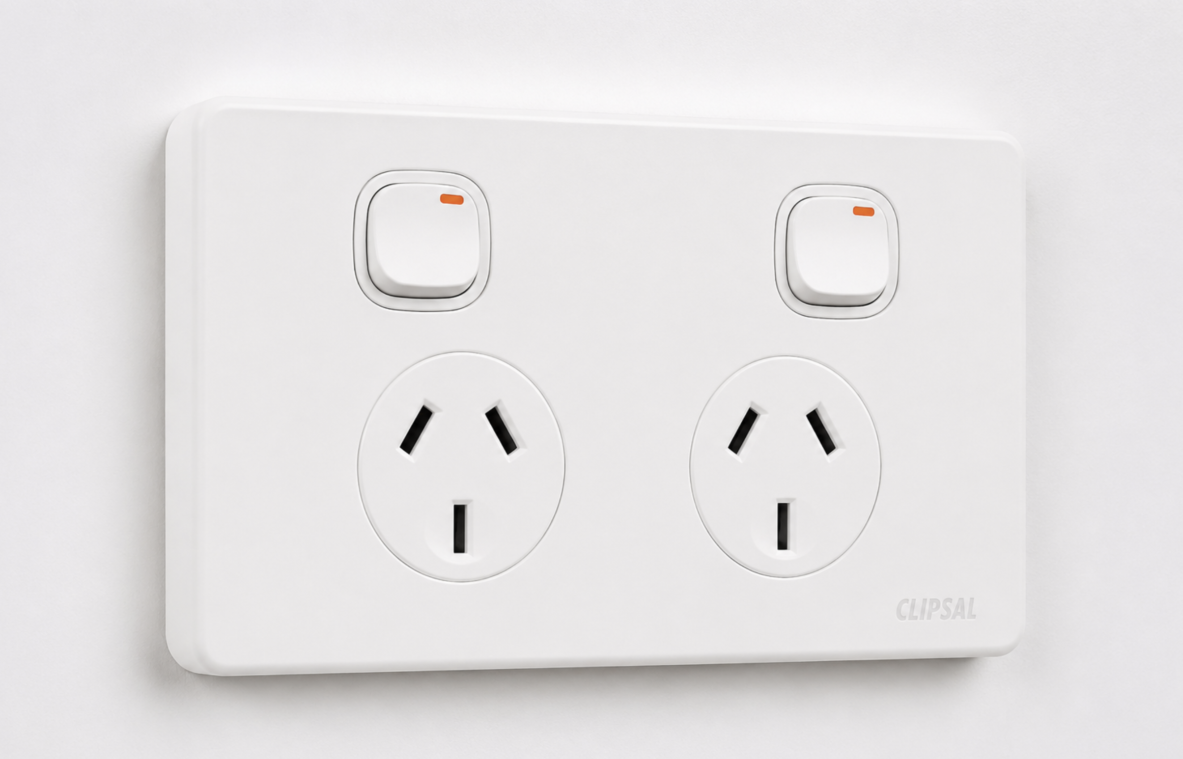 A white electrical power outlet with two sockets and two switches located above the sockets.