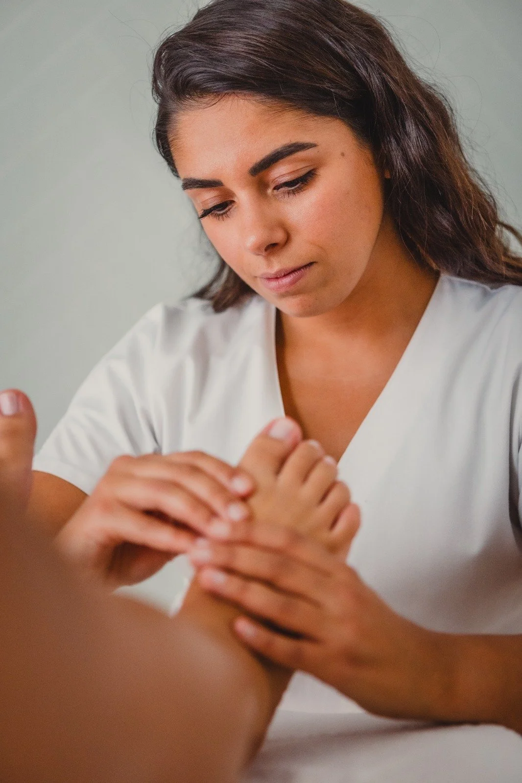 Une femme en uniforme blanc en train d'examiner ou de masser un pied.